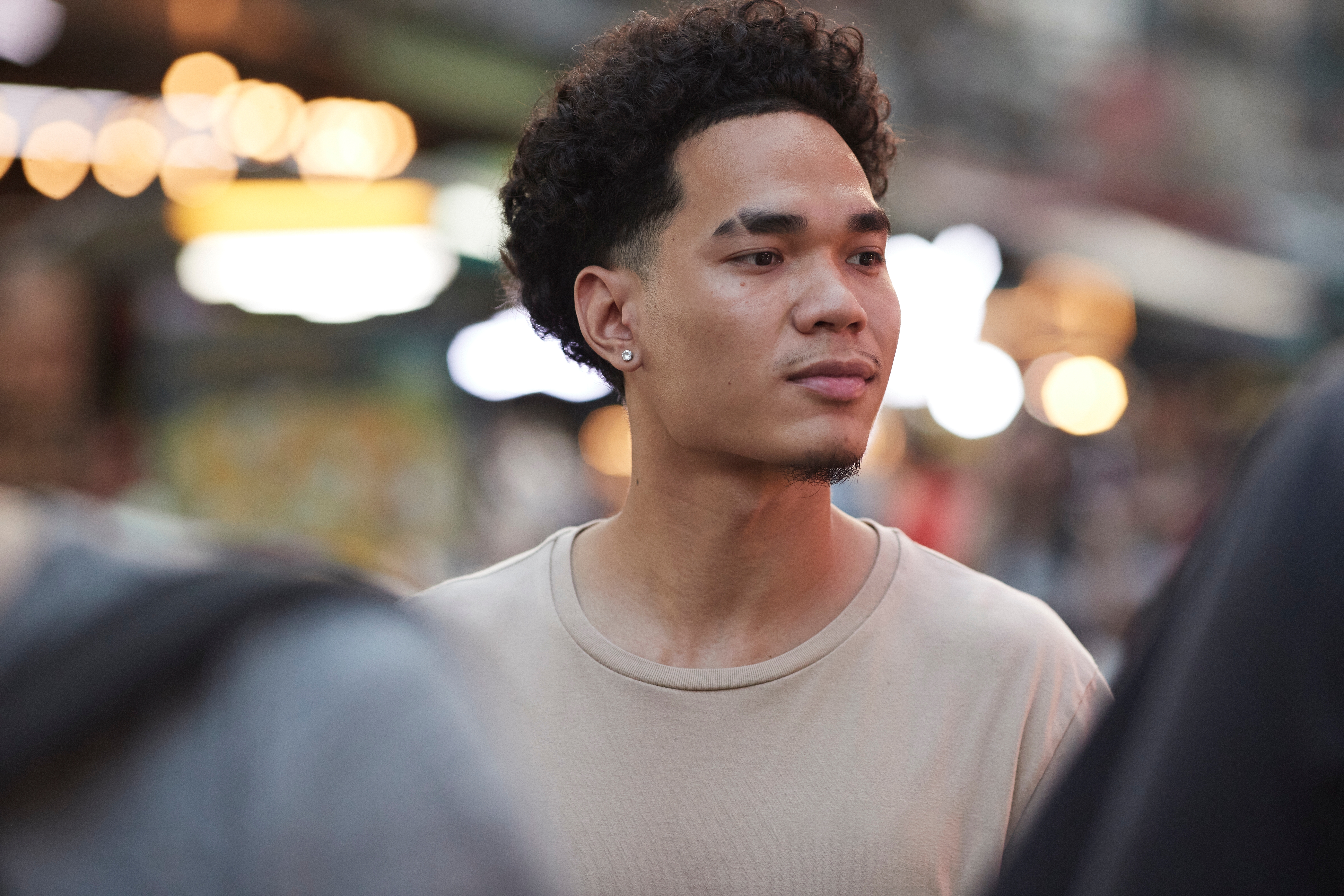 Person with short curly hair looks contemplative in a bustling street setting