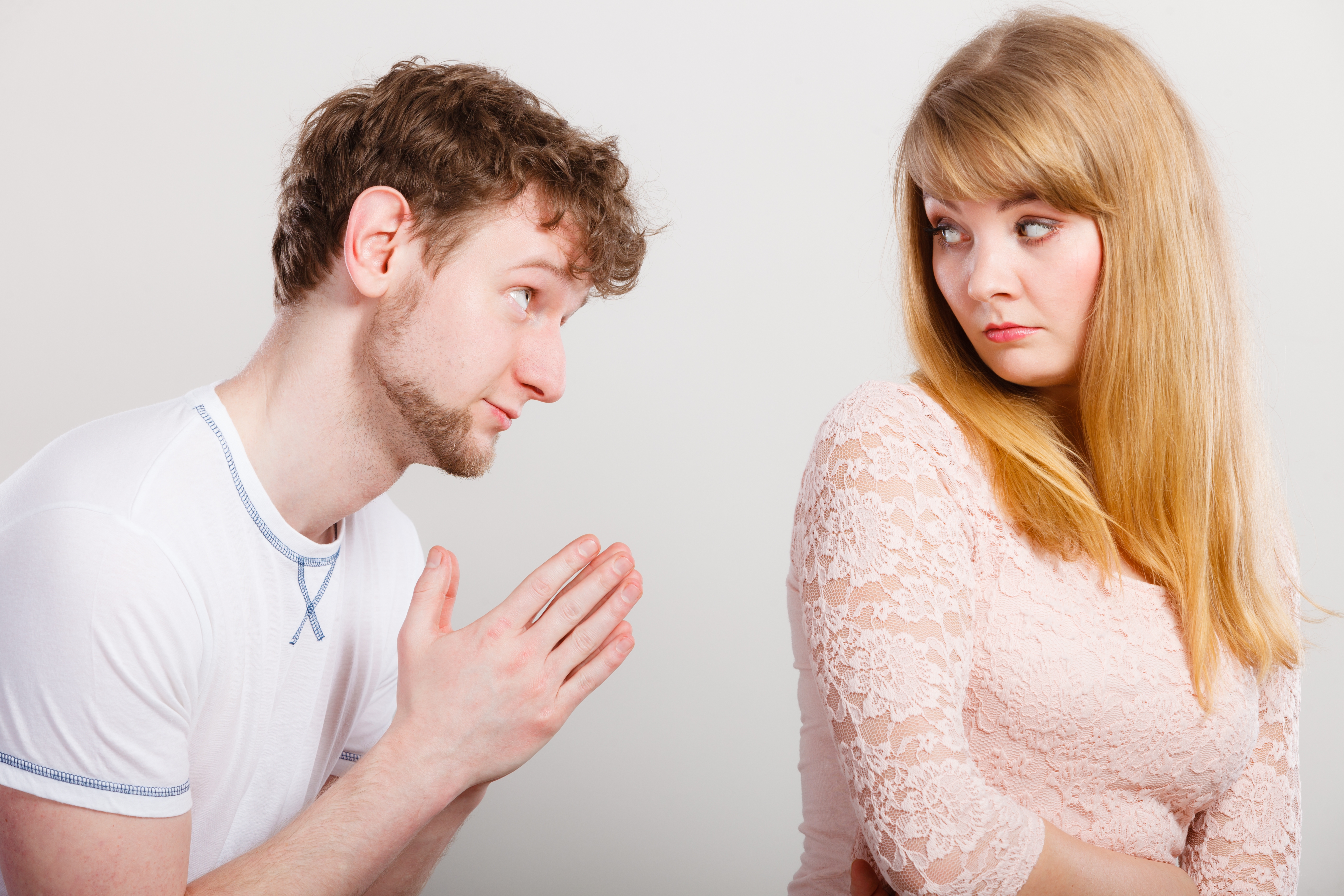 A man in a white tee shirt gestures apologetically towards a woman in a lace top who looks away, appearing upset