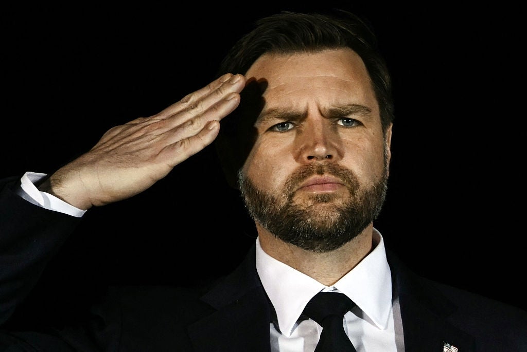 Person i dress og slips som hilser med et alvorlig uttrykk mot mørk bakgrunn