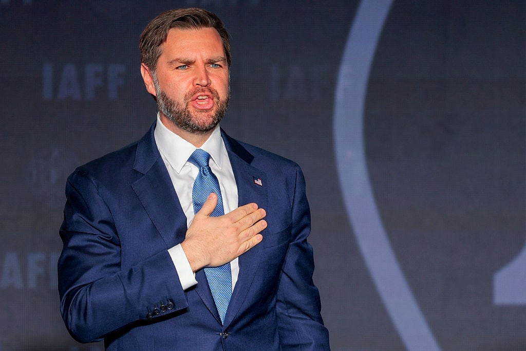 Mann i dress og slips snakker med hånd over hjerte på scenen