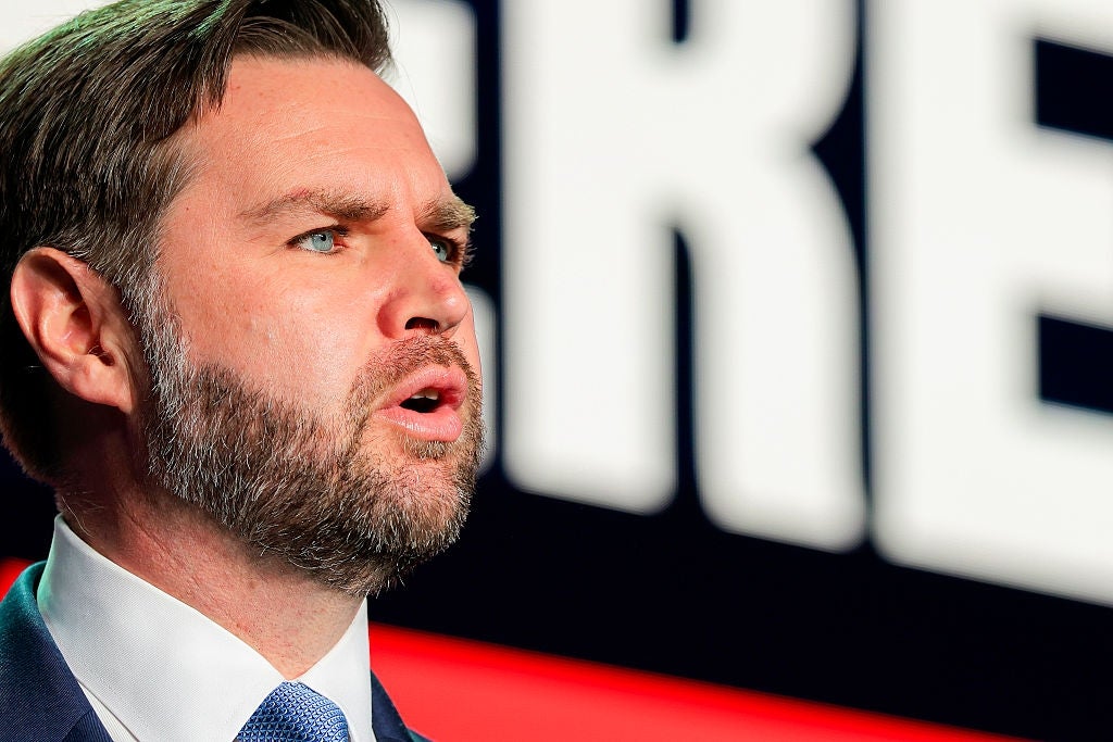 Mann i profesjonell antrekk snakker lidenskapelig på et arrangement. Bakgrunnen viser en del av en stor, uskarp tekst