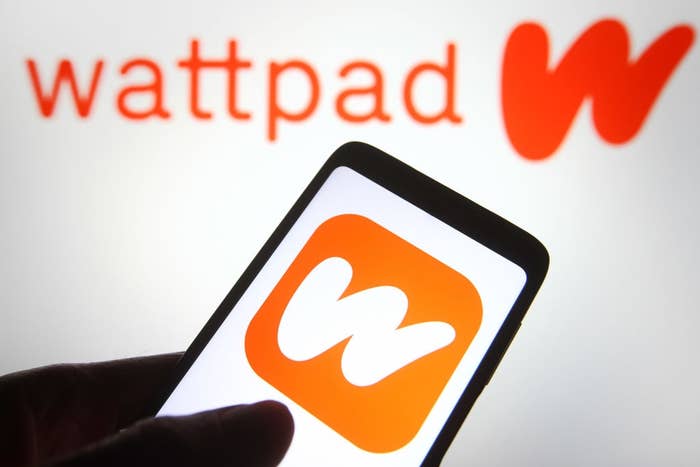 Hand holding a smartphone displaying the Wattpad logo connected  its screen, with the larger Wattpad logo successful  the background