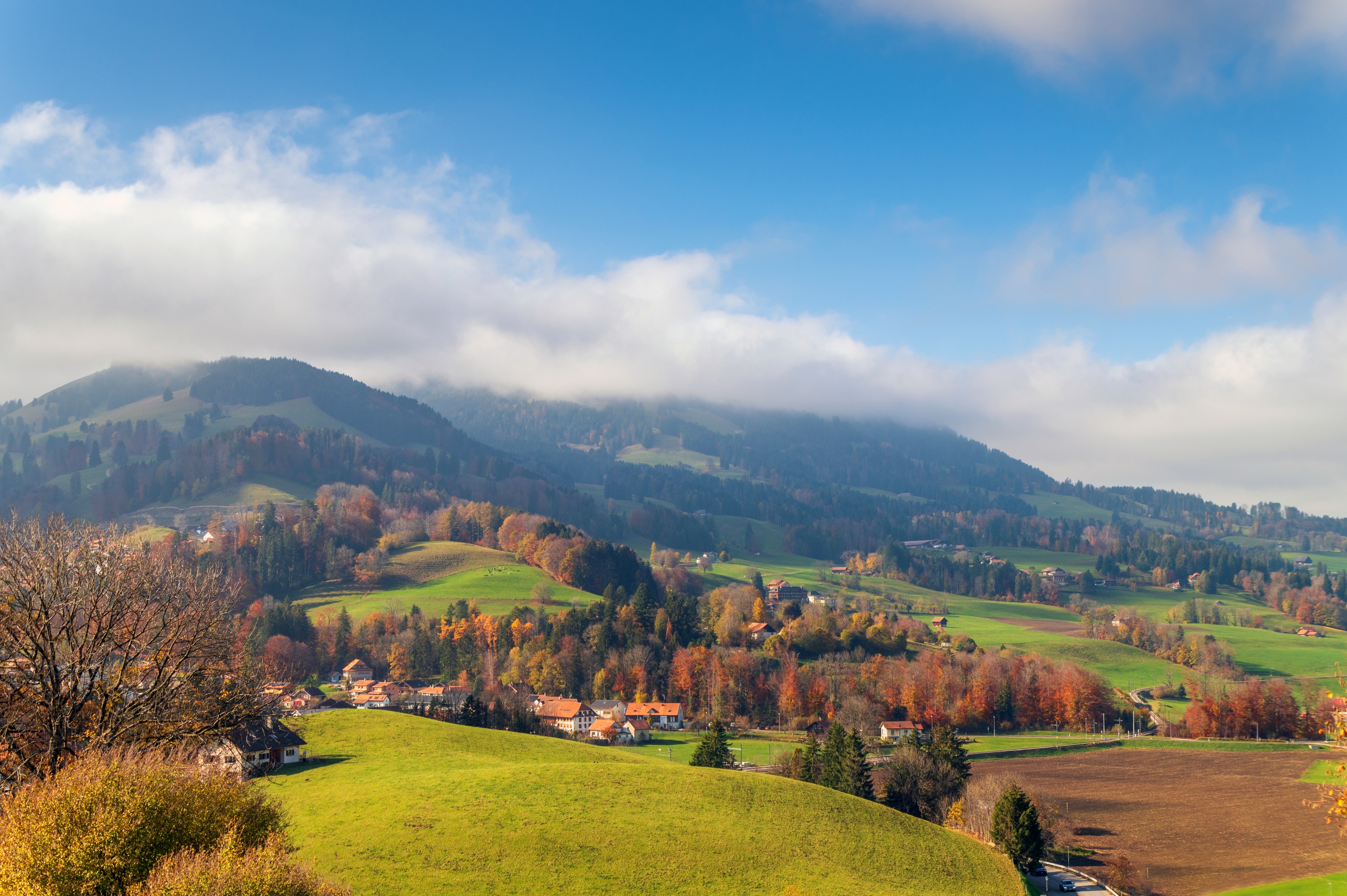 Scenic scenery  with rolling hills, a tiny  colony   nestled amidst autumn foliage, and mountains successful  the inheritance  nether  a partially  cloudy sky