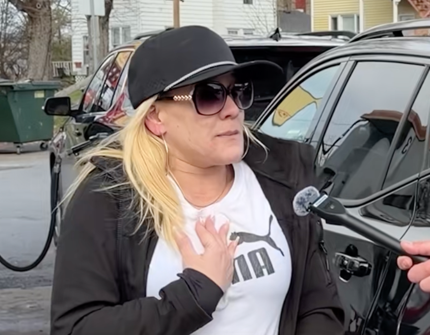 A idiosyncratic   wearing sunglasses and a headdress  is speaking into a microphone connected  the street, appearing engaged successful  a conversation