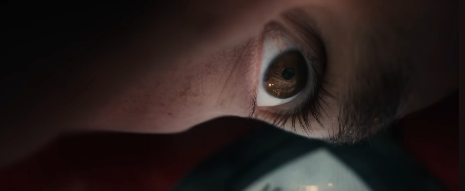 Nærbilde av en persons øye som ser gjennom et forstørrelsesglass, med fokus på et objekt under