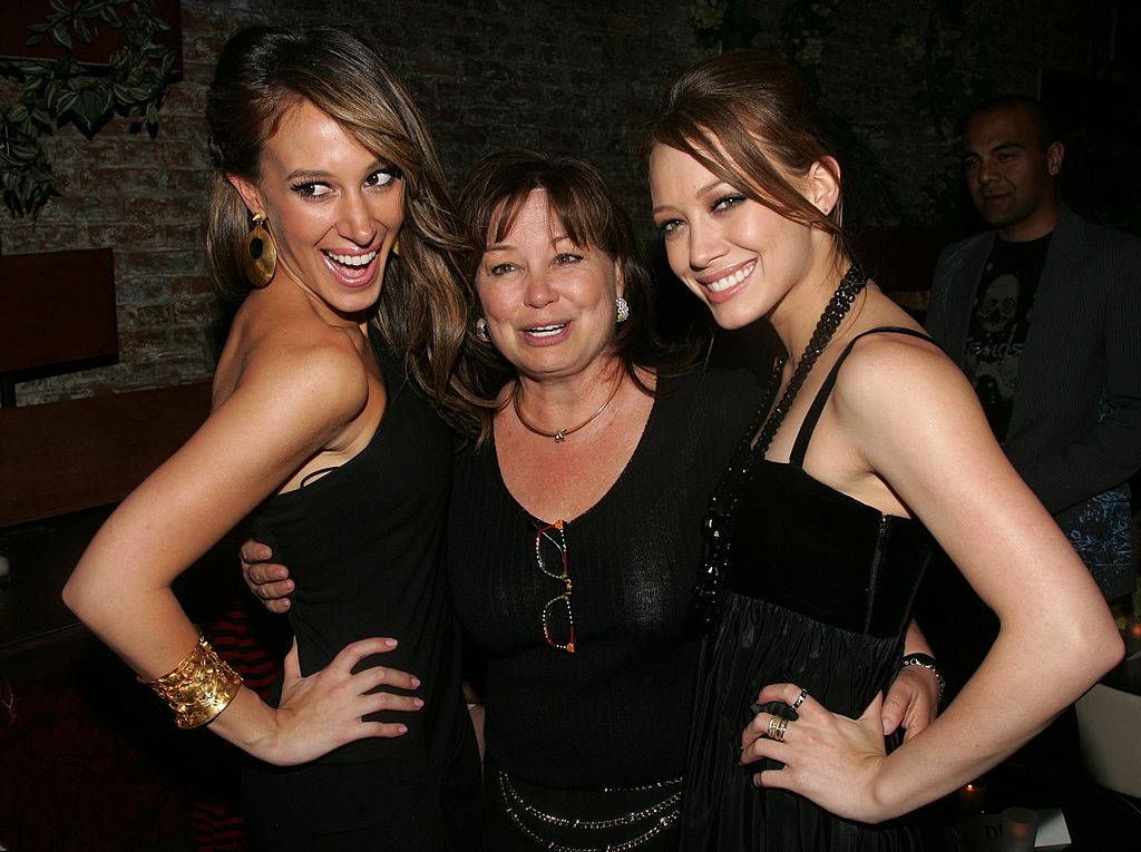 Three radical   smiling astatine  an event. Two women successful  elegant dresses with accessories basal   connected  either broadside  of a pistillate   successful  a casual top