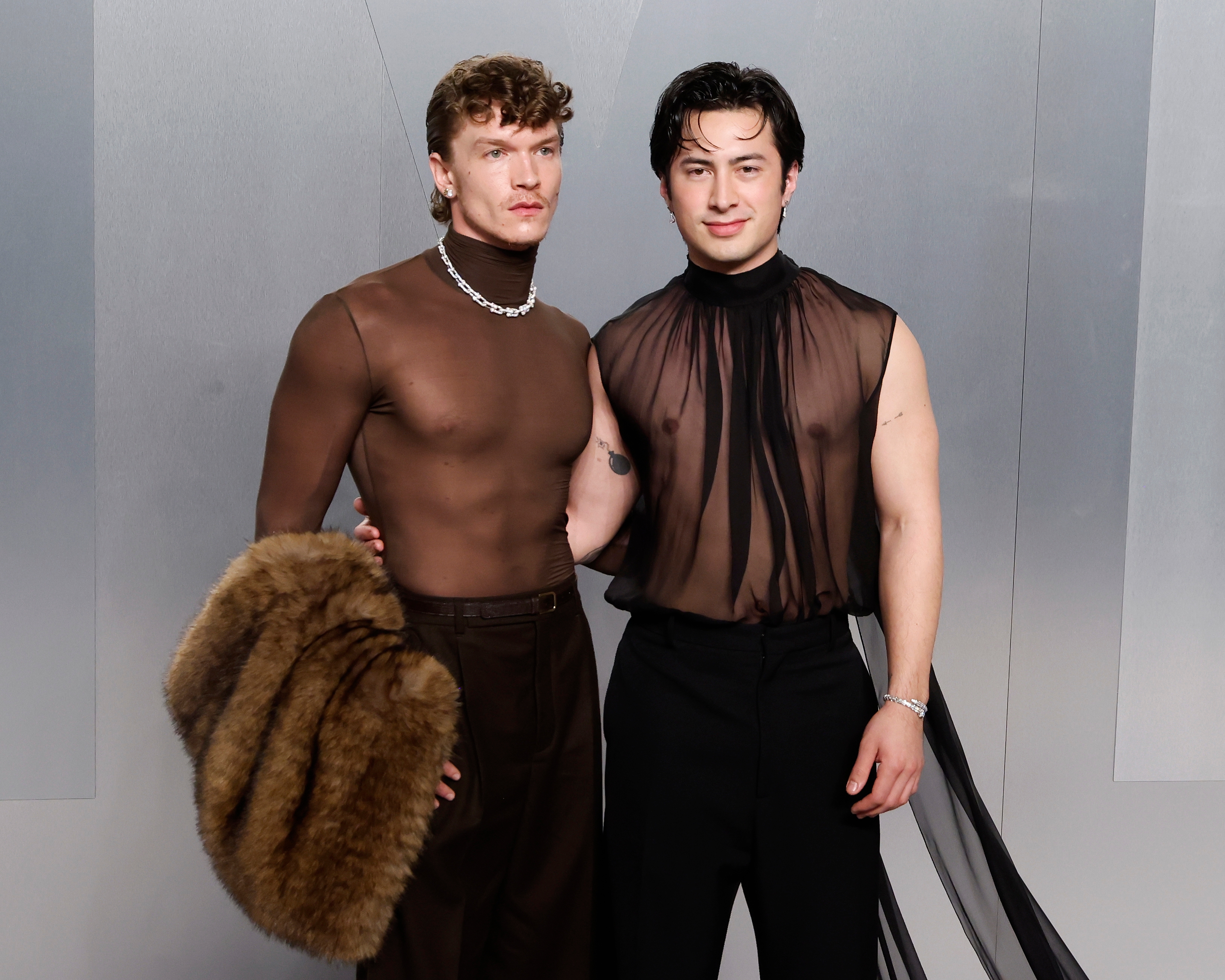 Two individuals connected  a reddish  carpet airs  side-by-side. One wears a sheer turtleneck and holds a fur accessory, portion    the different   dons a sheer flowing top