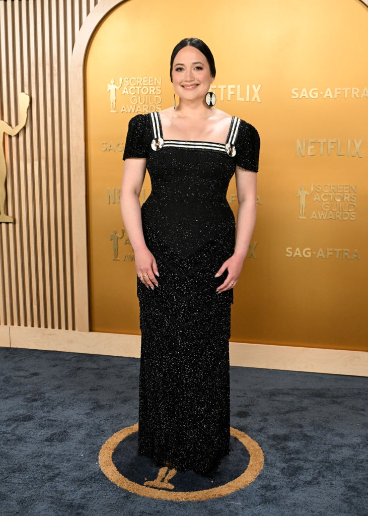 Lily connected  a reddish  carpet wears a fitted, sparkly gown with a quadrate  neckline and bold, matching earrings