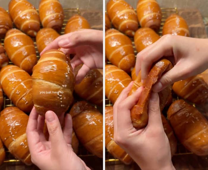 Hands holding a freshly baked buttery croissant with a sprinkle of coarse salt, surrounded by much  croissants connected  a cooling rack