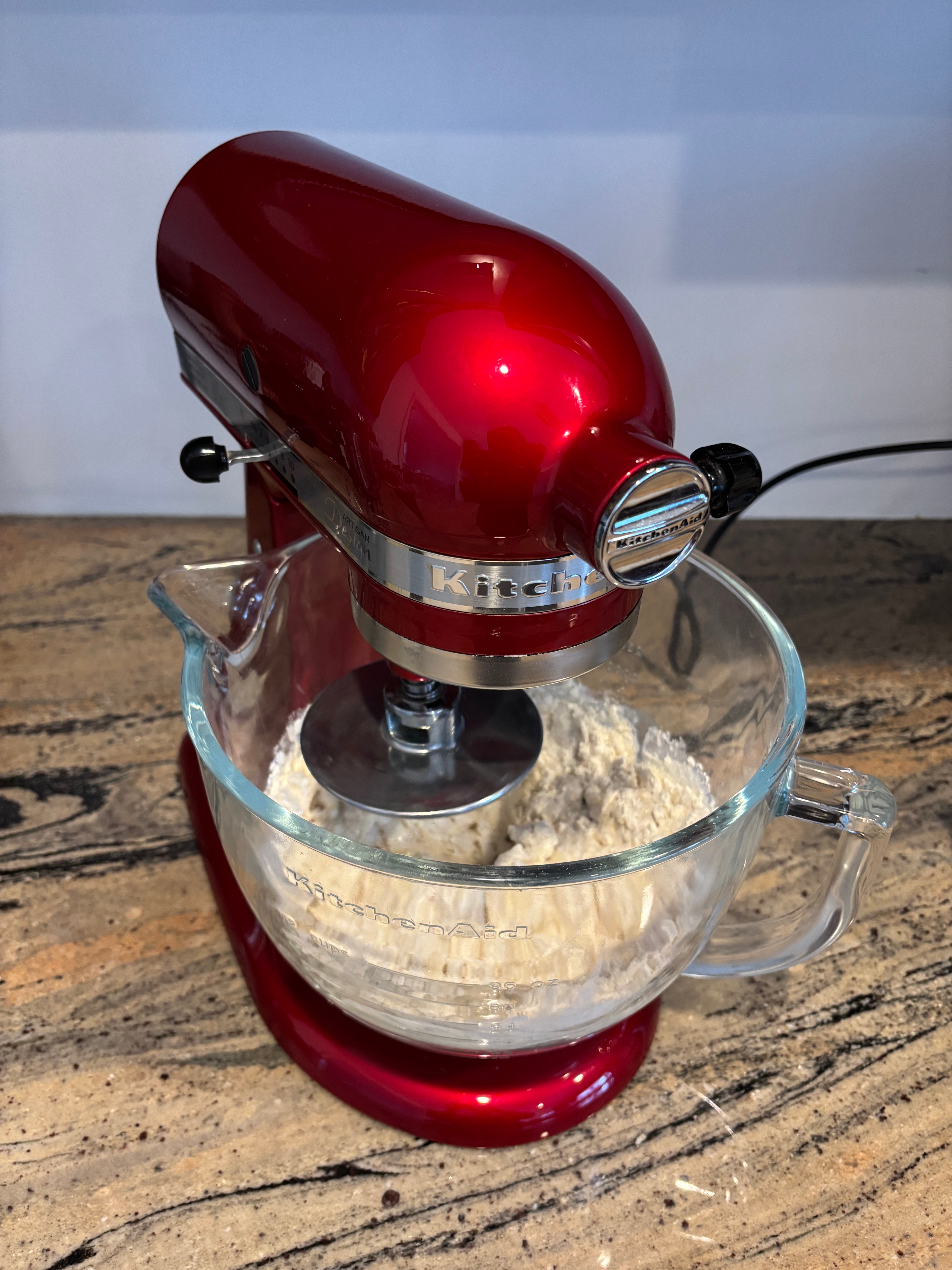A reddish  basal   mixer with a solid  vessel  is mixing flour connected  a room  countertop