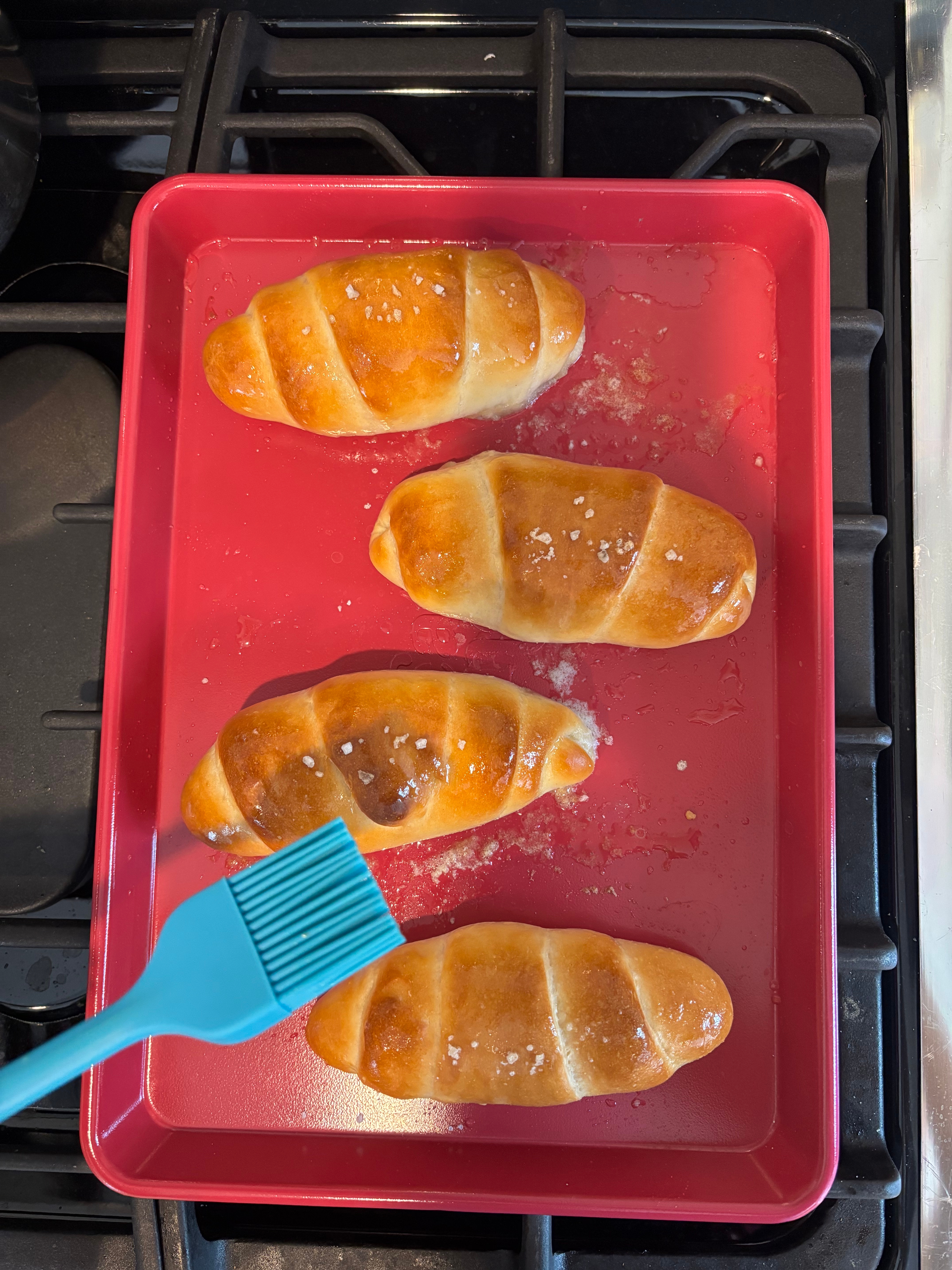 Four freshly baked croissants connected  a baking tray, brushed with food  and sprinkled with salt