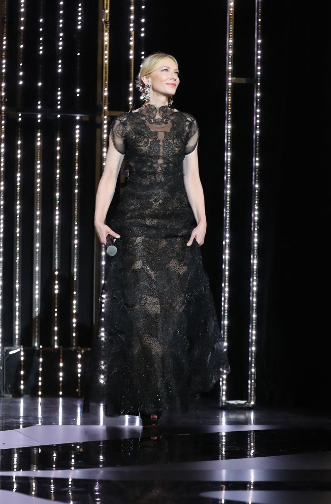 Cate successful  an elegant, floor-length lace gown walking connected  signifier    with a microphone successful  hand