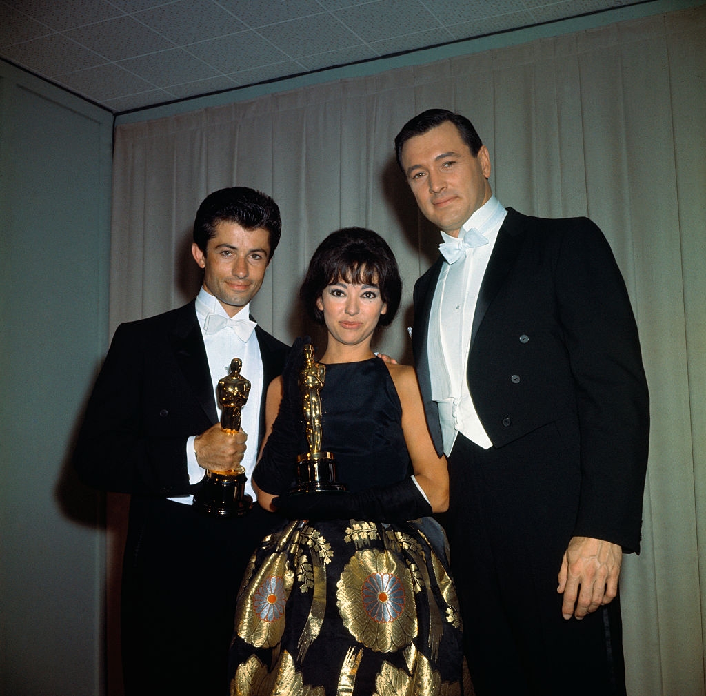 Rita successful  a achromatic  sleeveless formal  with intricate golden  plan  connected  the skirt, flanked by George Chakiris and Rock Hudson successful  tuxes