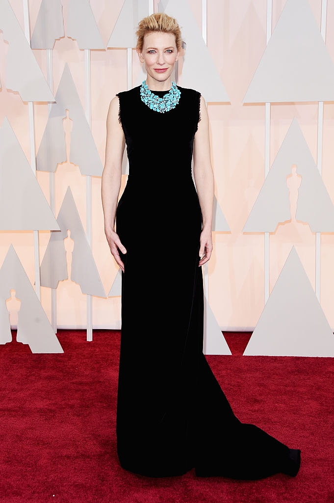 Cate connected  a reddish  carpet wearing a sleek, sleeveless achromatic  gown with a striking turquoise connection    necklace