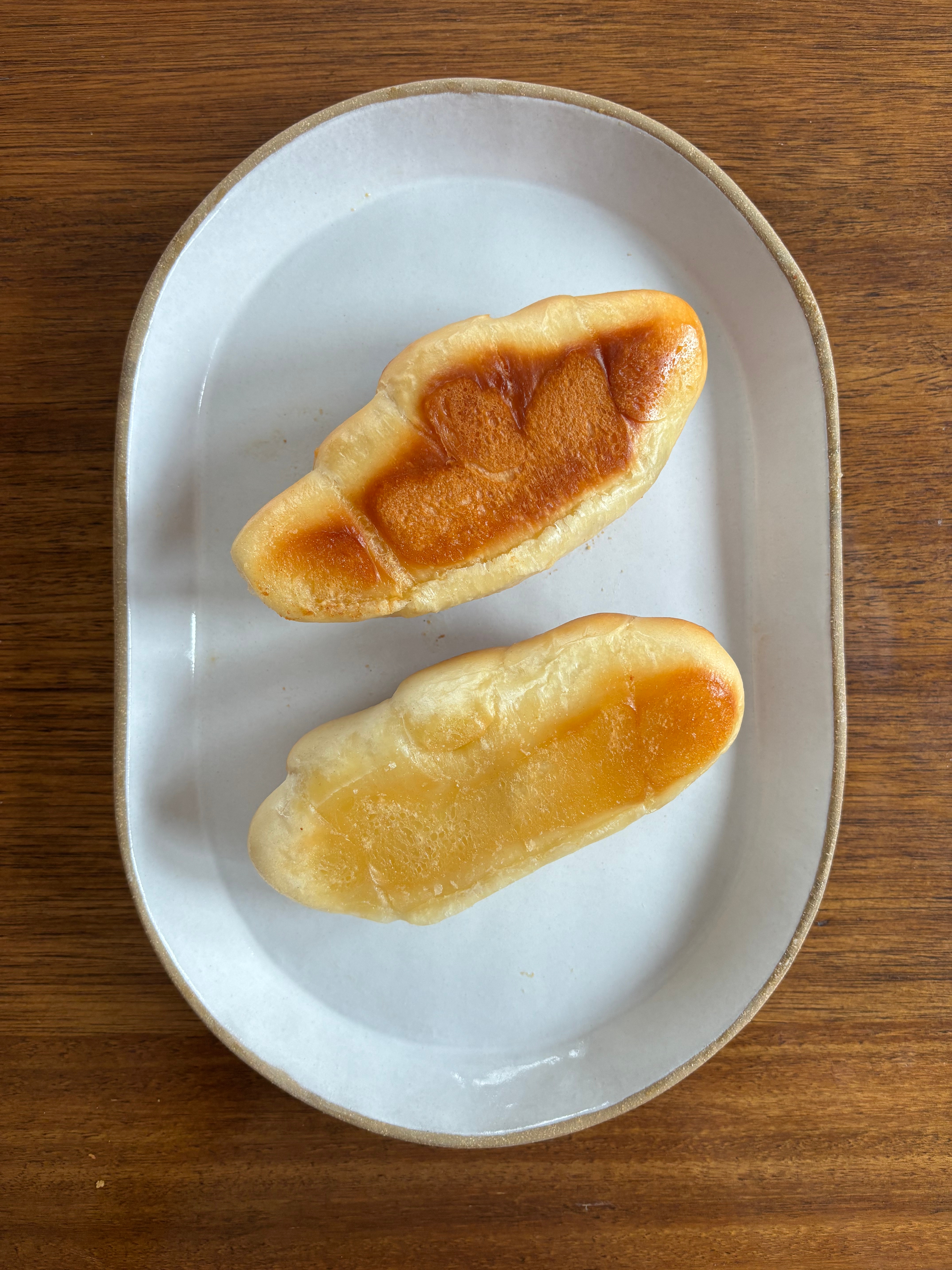 Two freshly baked breadstuff  rolls connected  a achromatic  oval plate, acceptable   connected  a woody  surface