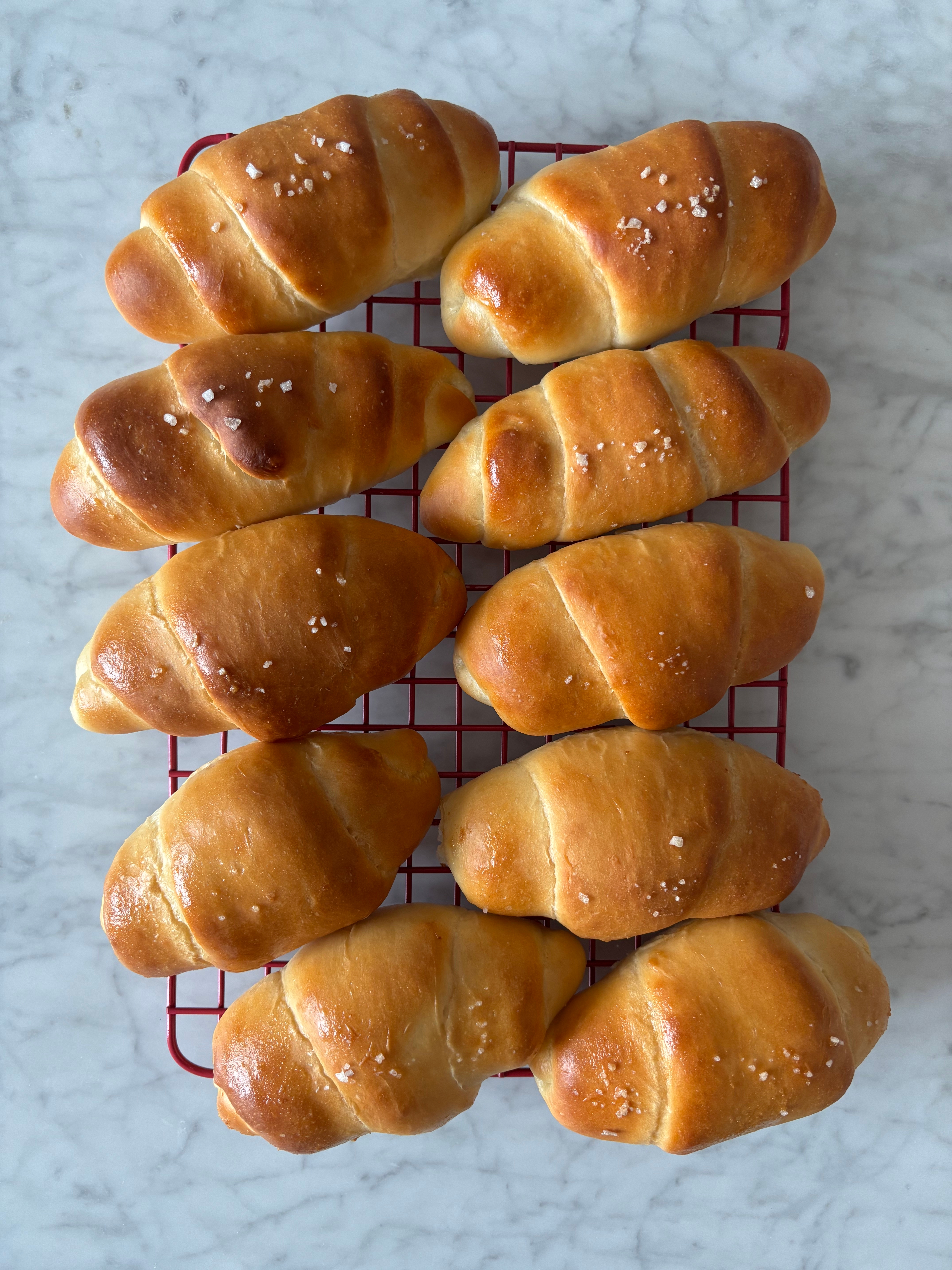 Freshly baked crescent rolls arranged connected  a cooling rack, sprinkled with coarse salt