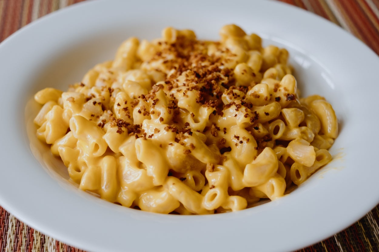 A bowl of creamy macaroni and cheese topped with breadcrumbs on a striped tablecloth