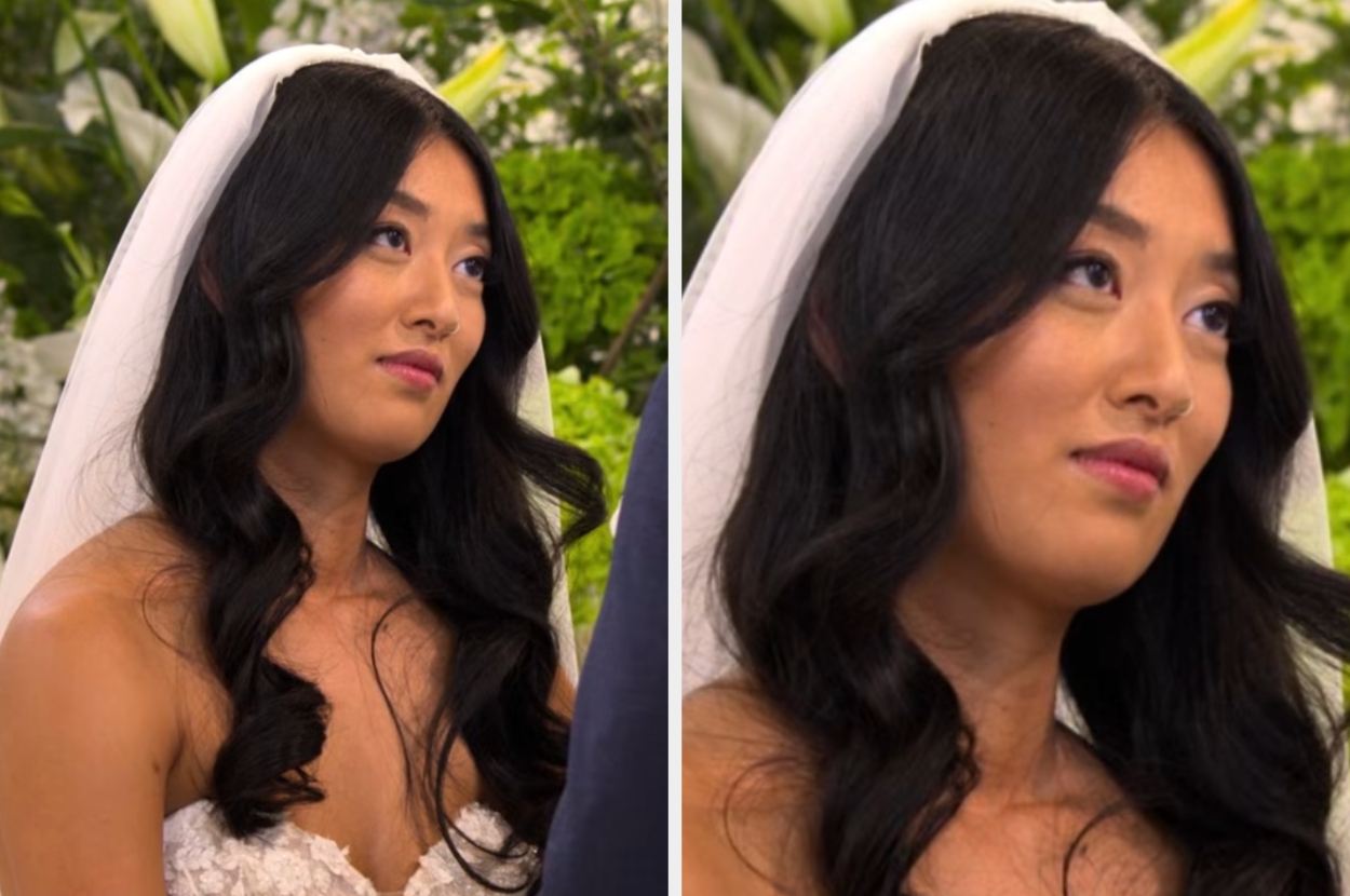 Bride in lace wedding gown with veil, smiling softly during ceremony amidst a backdrop of lush greenery