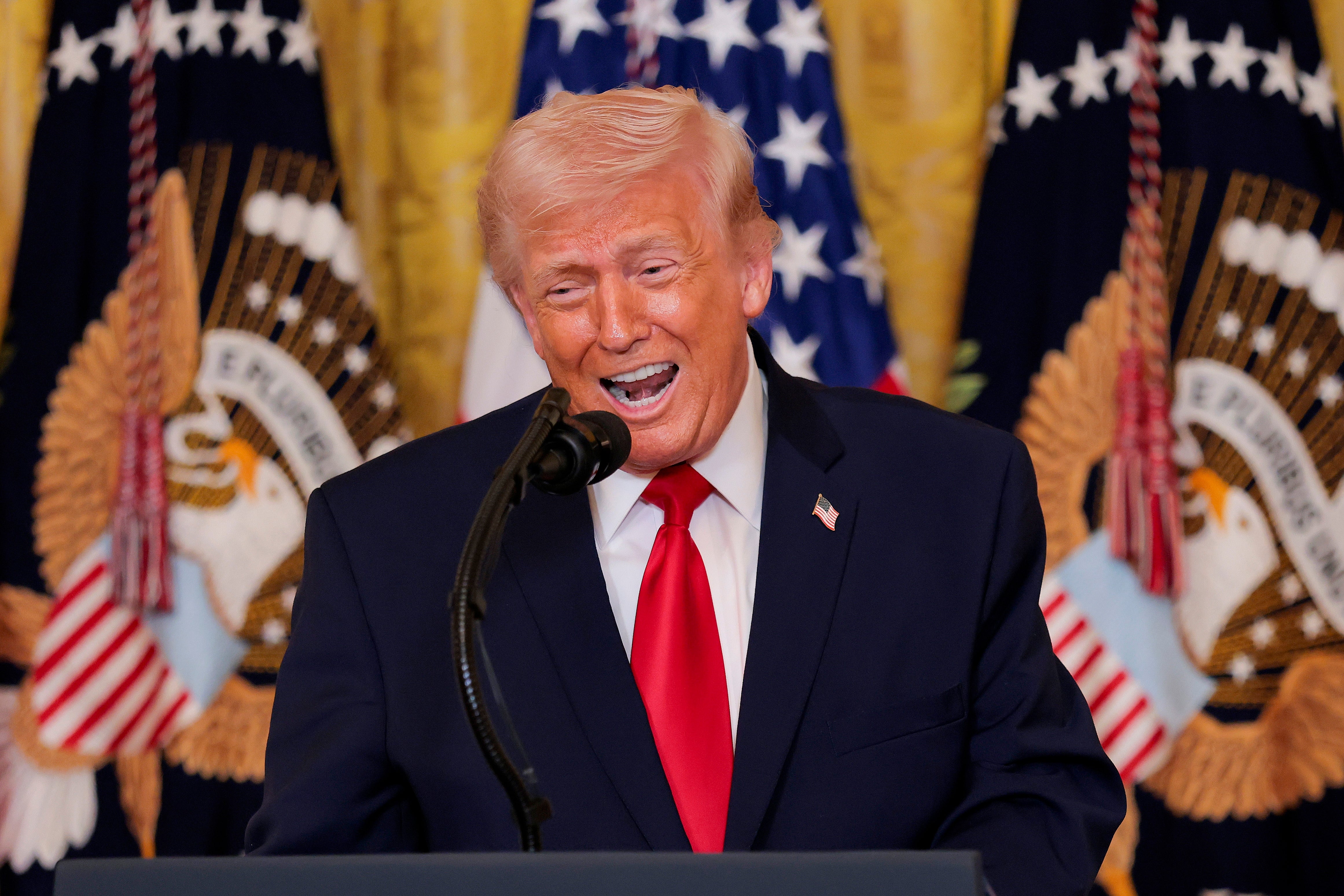 En mann snakker på et podium med amerikanske flagg i bakgrunnen, iført dress og slips