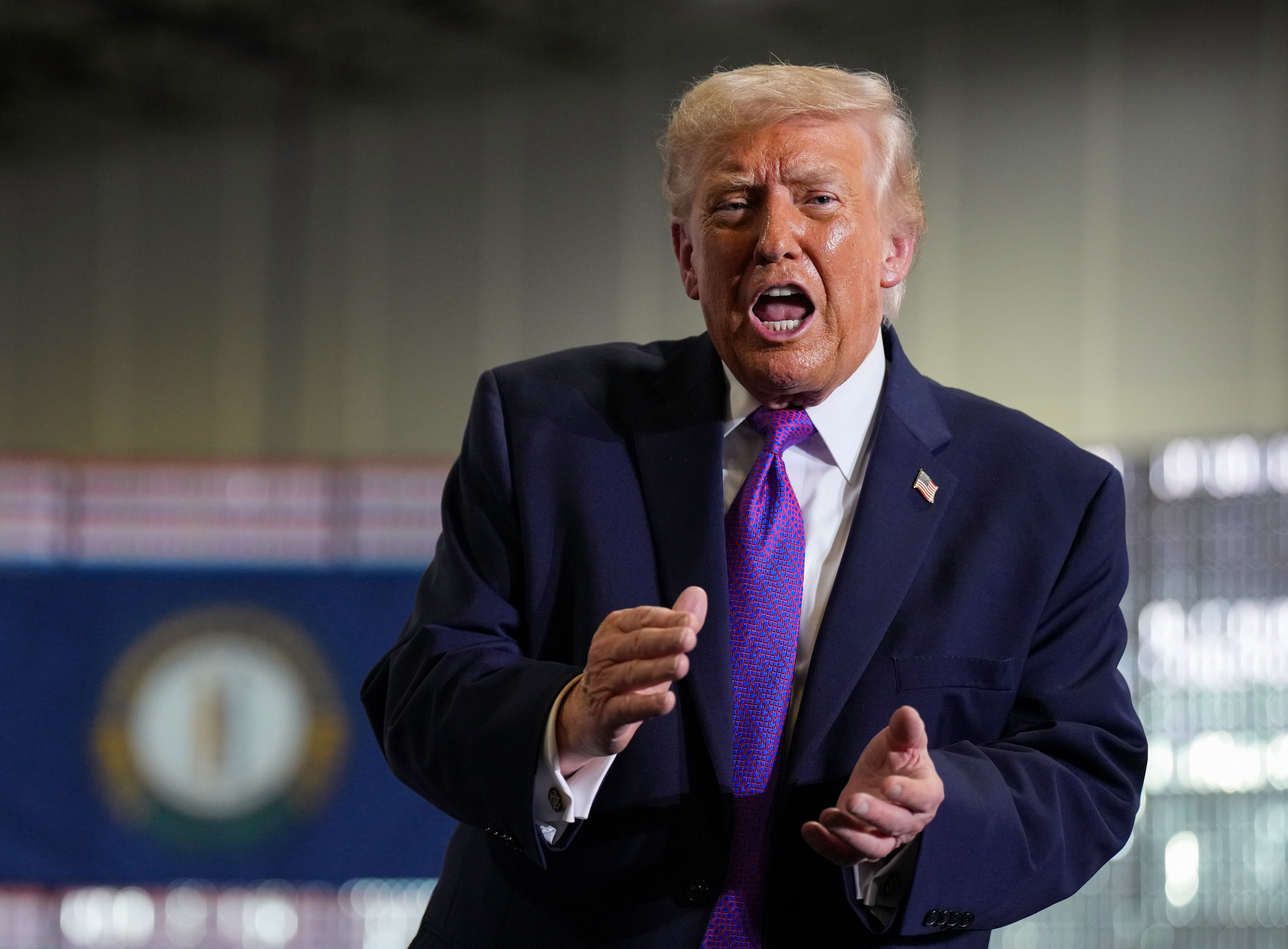 En person i dress og slips snakker energisk med uttrykksfulle bevegelser ved et arrangement