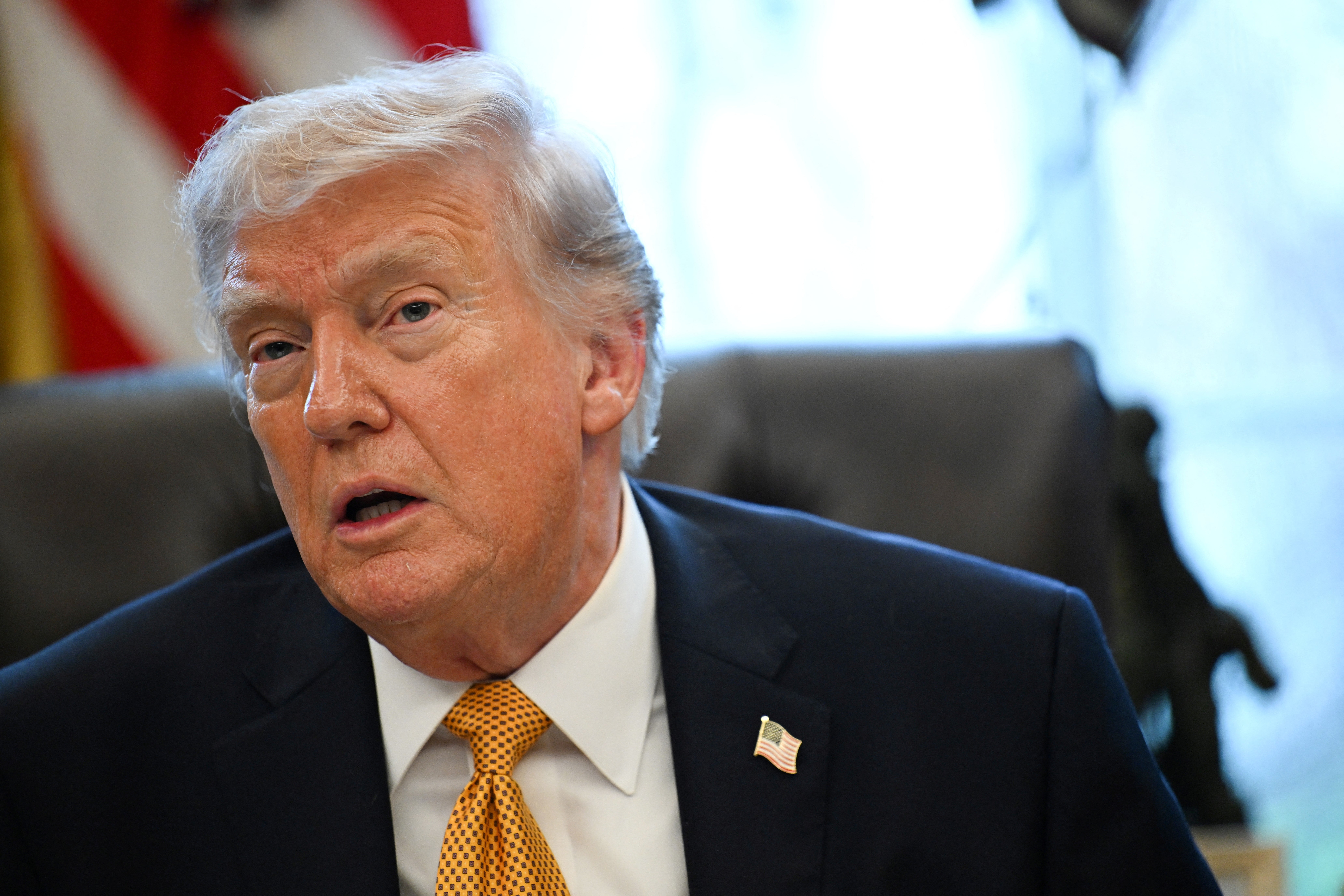 En mann i dress og slips sitter ved et skrivebord og ser ut til å snakke eller lytte, med et bekymret uttrykk