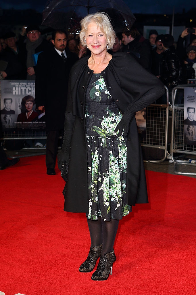 Helen connected  reddish  carpet wearing a floral formal  and coat, smiling with manus  connected  hip. Crowd and posters successful  background
