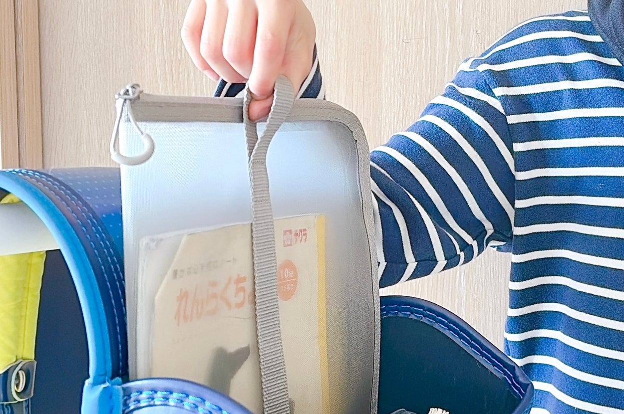 ランドセルからファイルを取り出す子ども。ストライプ柄の服を着ている。