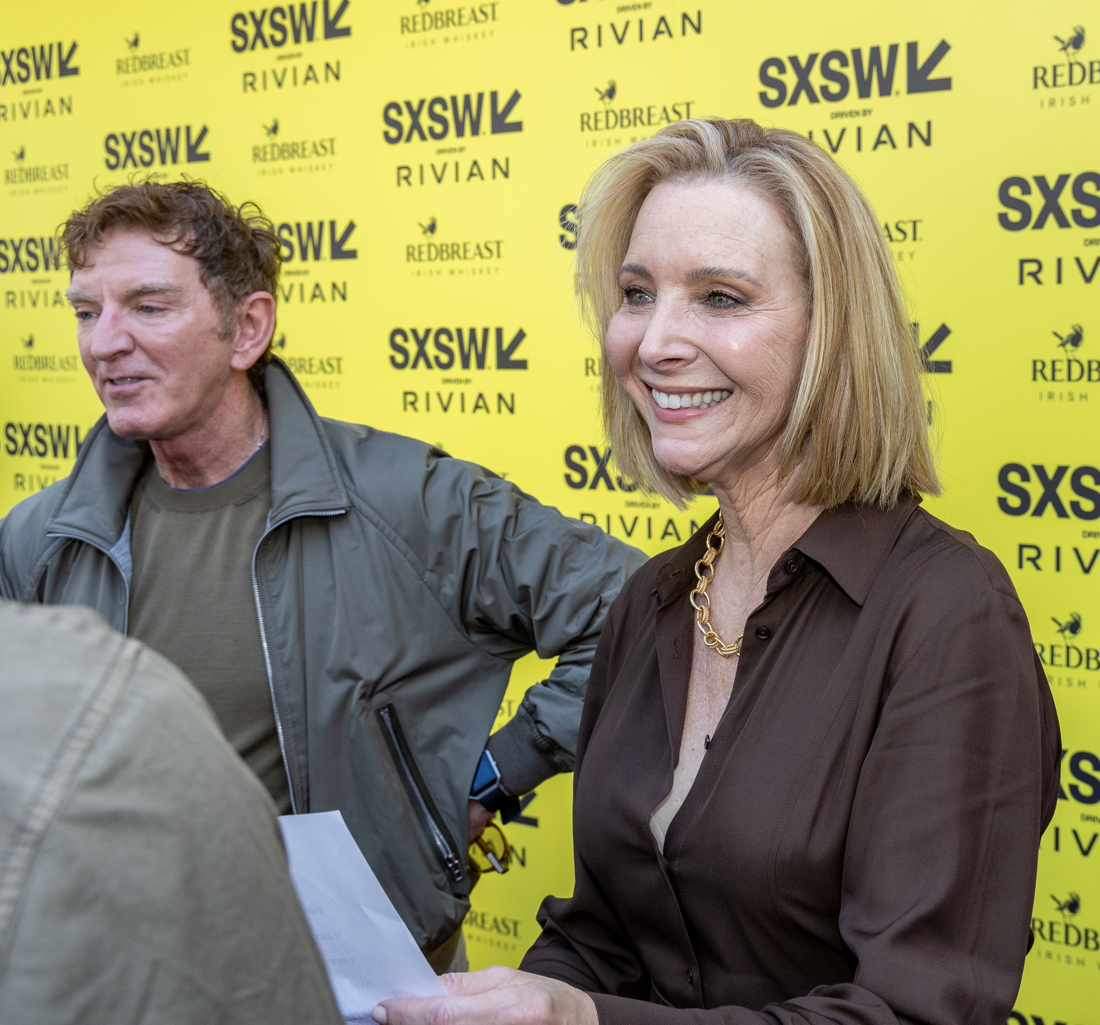 Two individuals astatine  a SXSW event; 1  smiles successful  elegant attire portion    the different   stands beside successful  casual deterioration  against a branded backdrop
