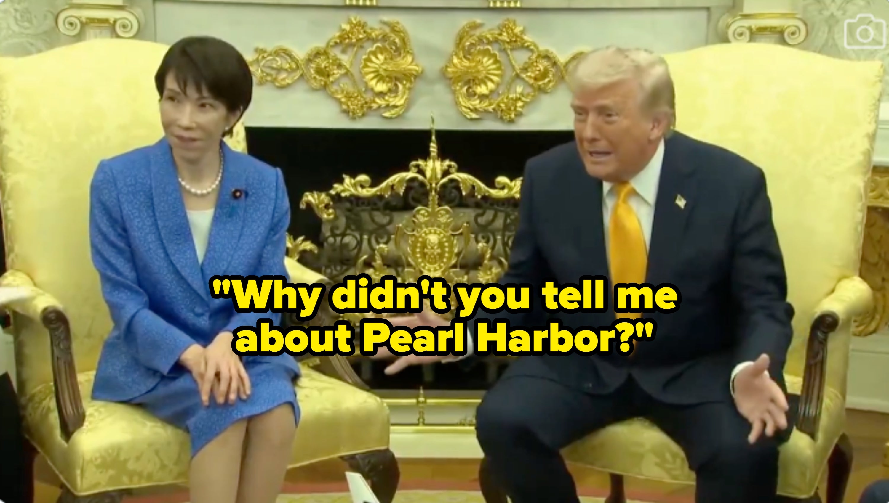 To personer som sitter i et utsmykket rom, en i blå dress og den andre i mørk dress med gult slips, ser ut til å være i samtale