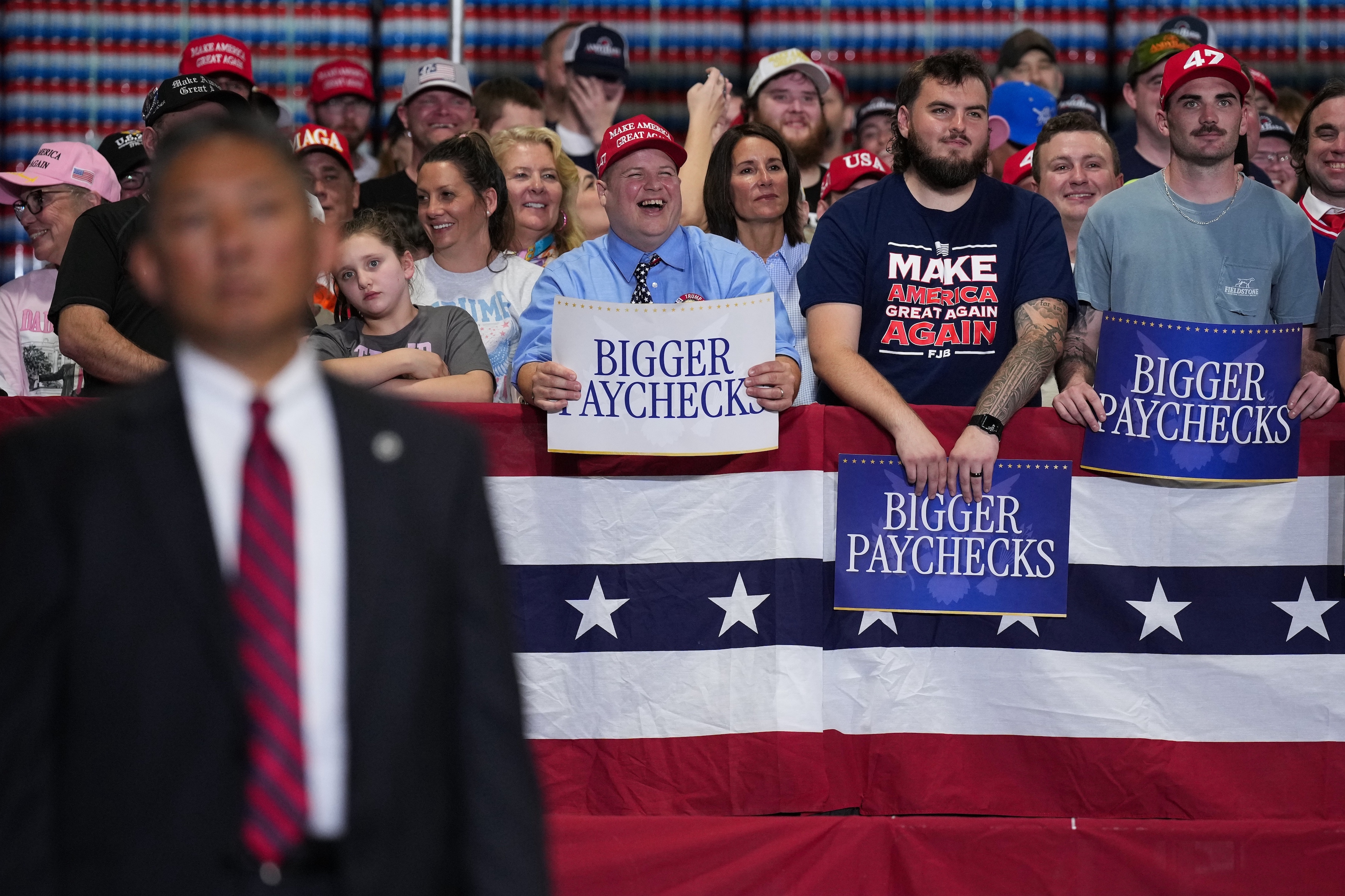 Group astatine a rally holding "Bigger Paychecks" signs, with a information idiosyncratic successful foreground and USA-themed decorations successful the background