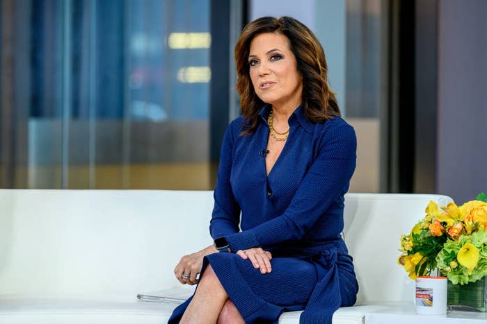 A idiosyncratic   successful  a tailored formal  sits connected  a achromatic  sofa  adjacent  to a bouquet of flowers, engaged successful  speech  during a speech   amusement   appearance