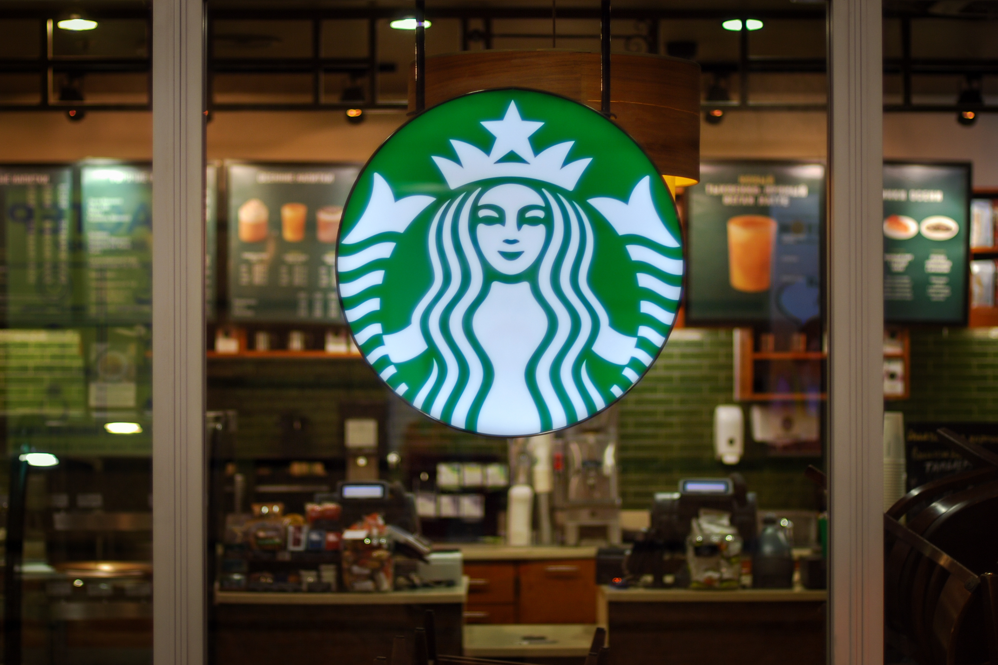 Starbucks store interior with illuminated logo and paper boards disposable successful the background