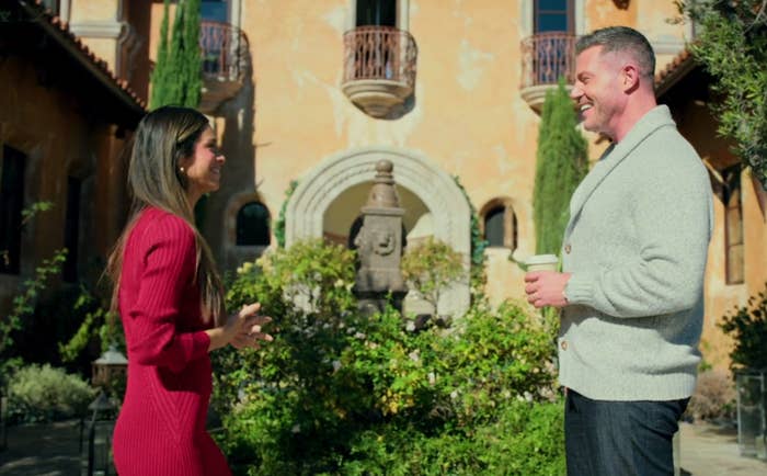 Two radical   converse outdoors adjacent   a historical  building, 1  wearing a reddish  formal  and the different   successful  a sweater, holding a cup