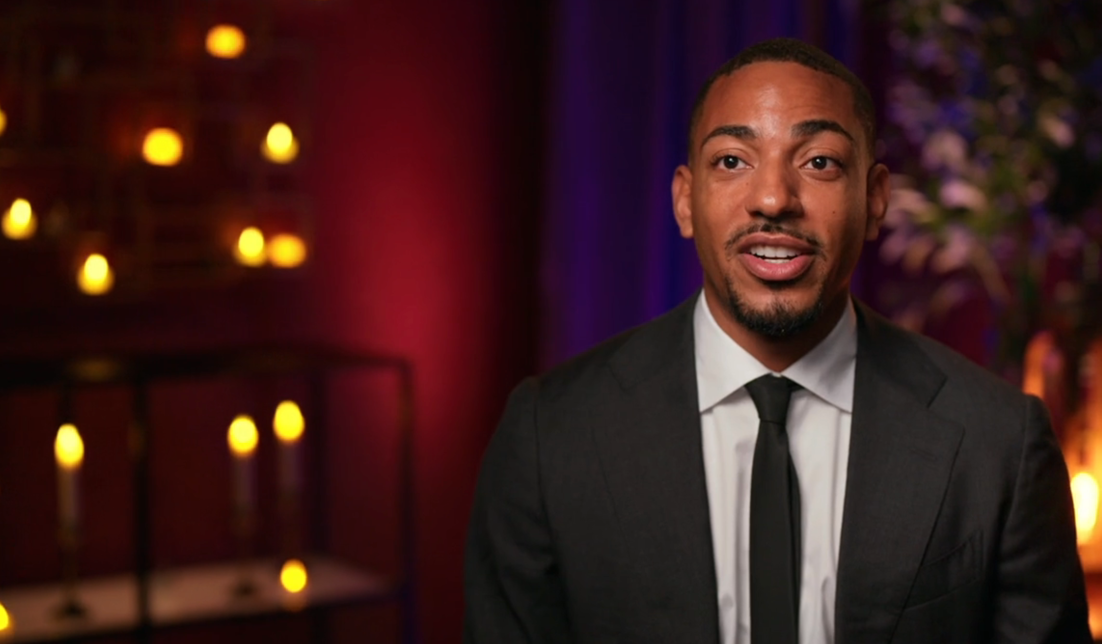 En person i dress og slips snakker i et levende lys, vendt mot kameraet