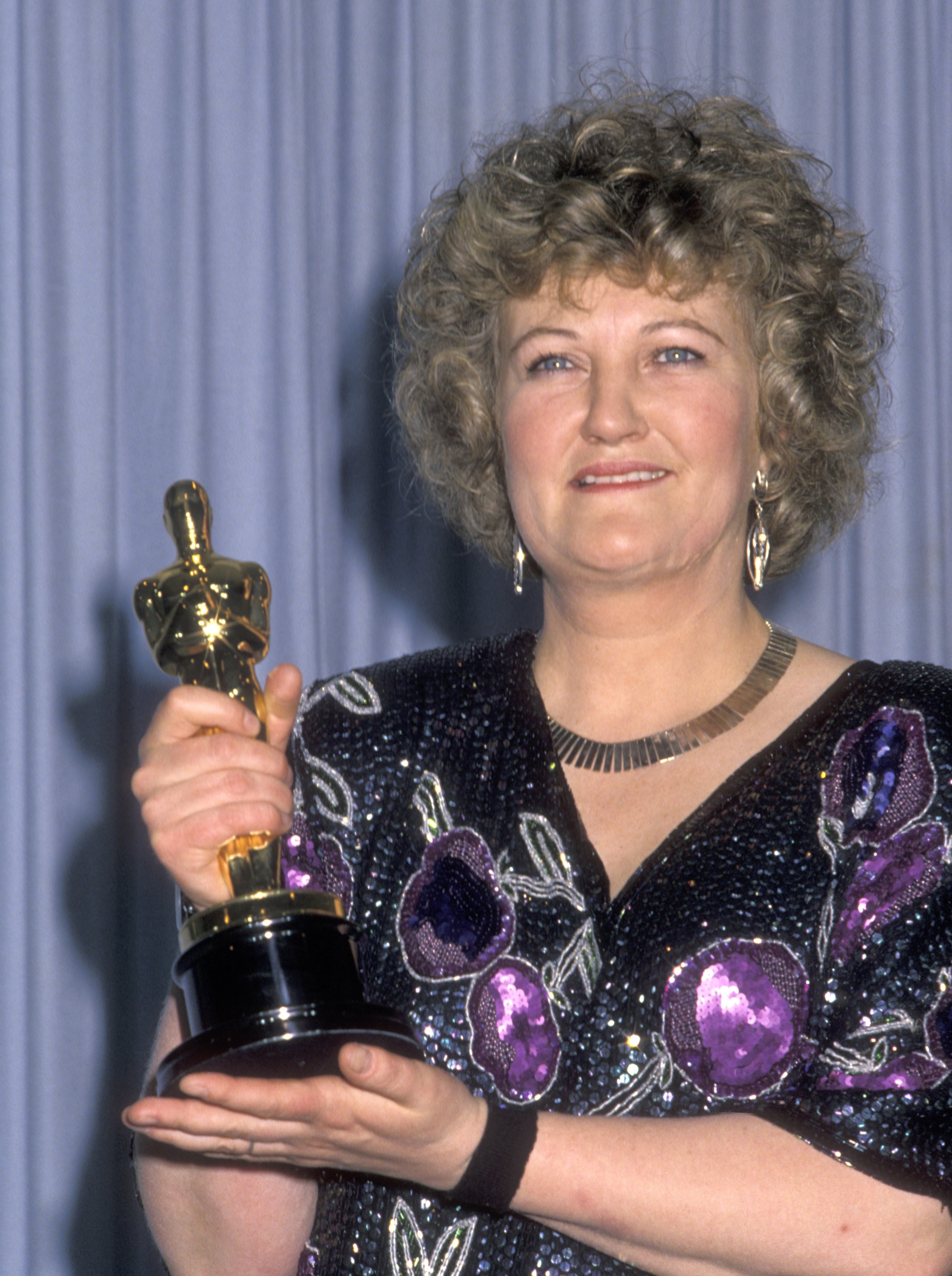 Brenda Fricker holding an Oscar, wearing an elaborately patterned gown with abstract designs and large earrings