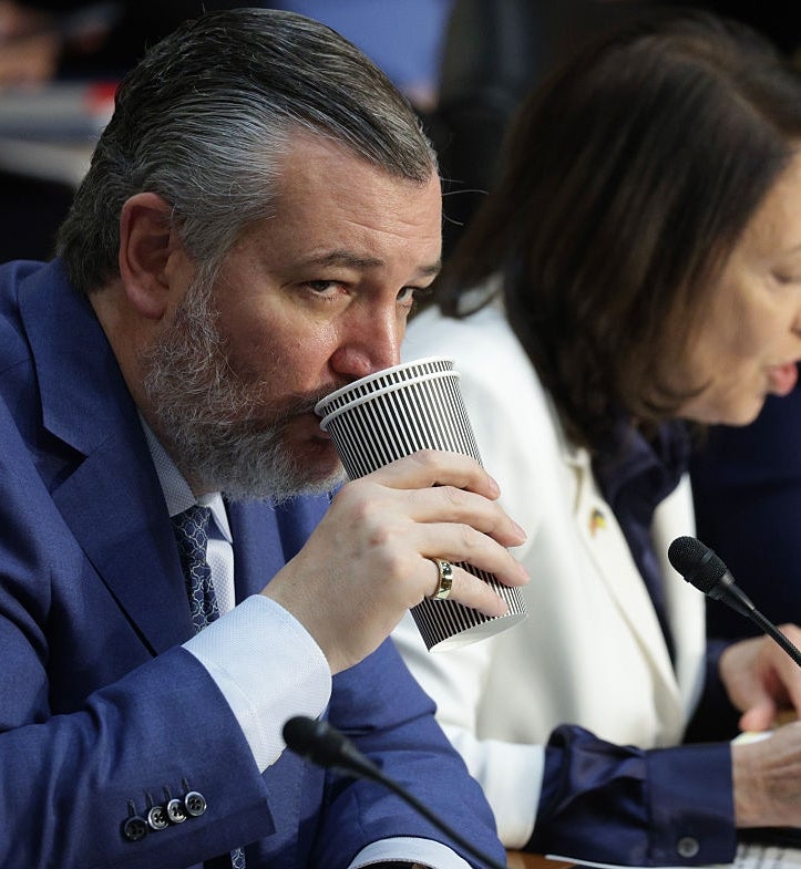 Person i dress som drikker fra en stripet kopp ved en formell begivenhet, ved siden av en annen person som snakker i en mikrofon