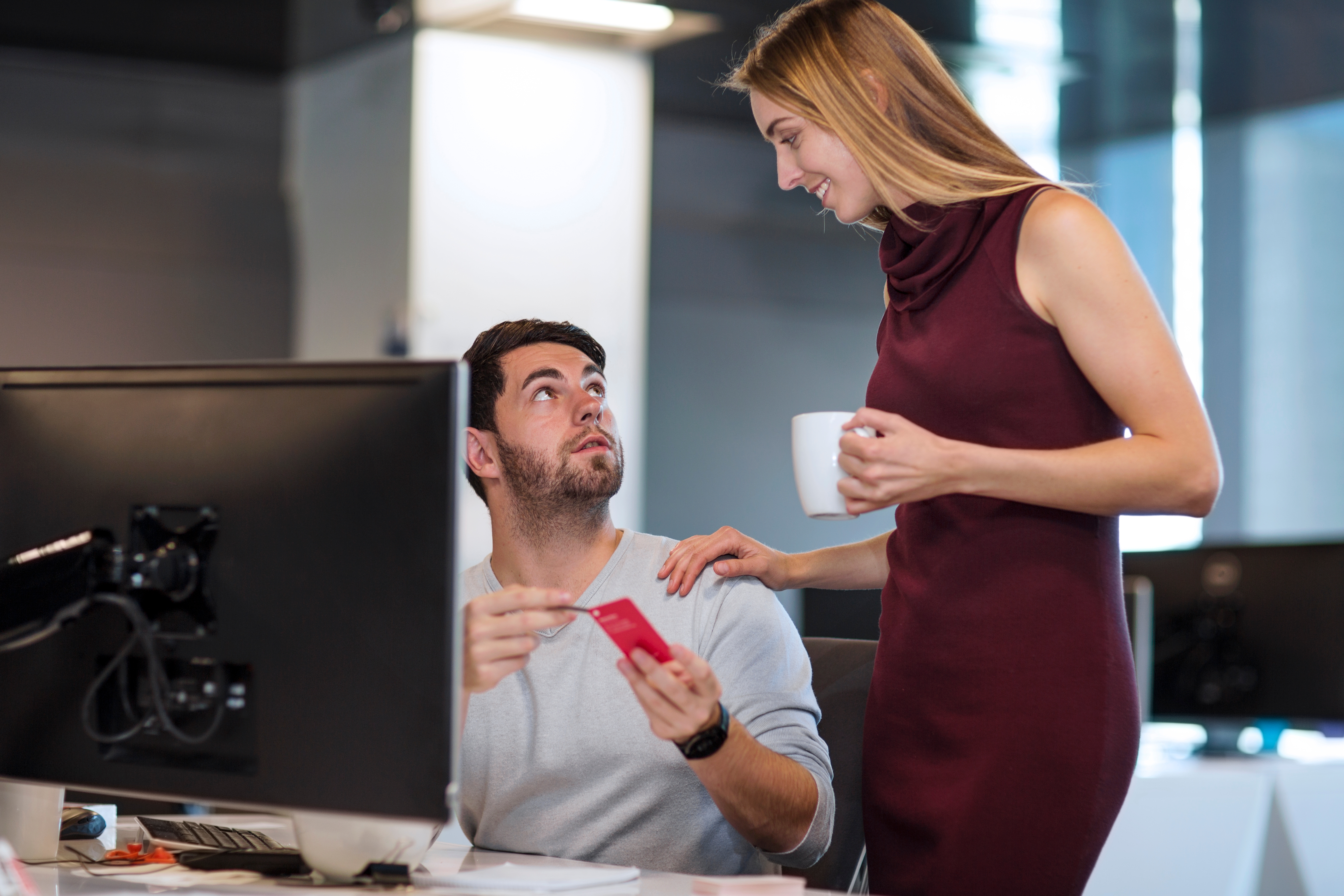 A antheral   seated astatine  a table  with a machine  holds a card, looking up   astatine  a lasting  pistillate   holding a mug, successful  a modern   bureau   setting