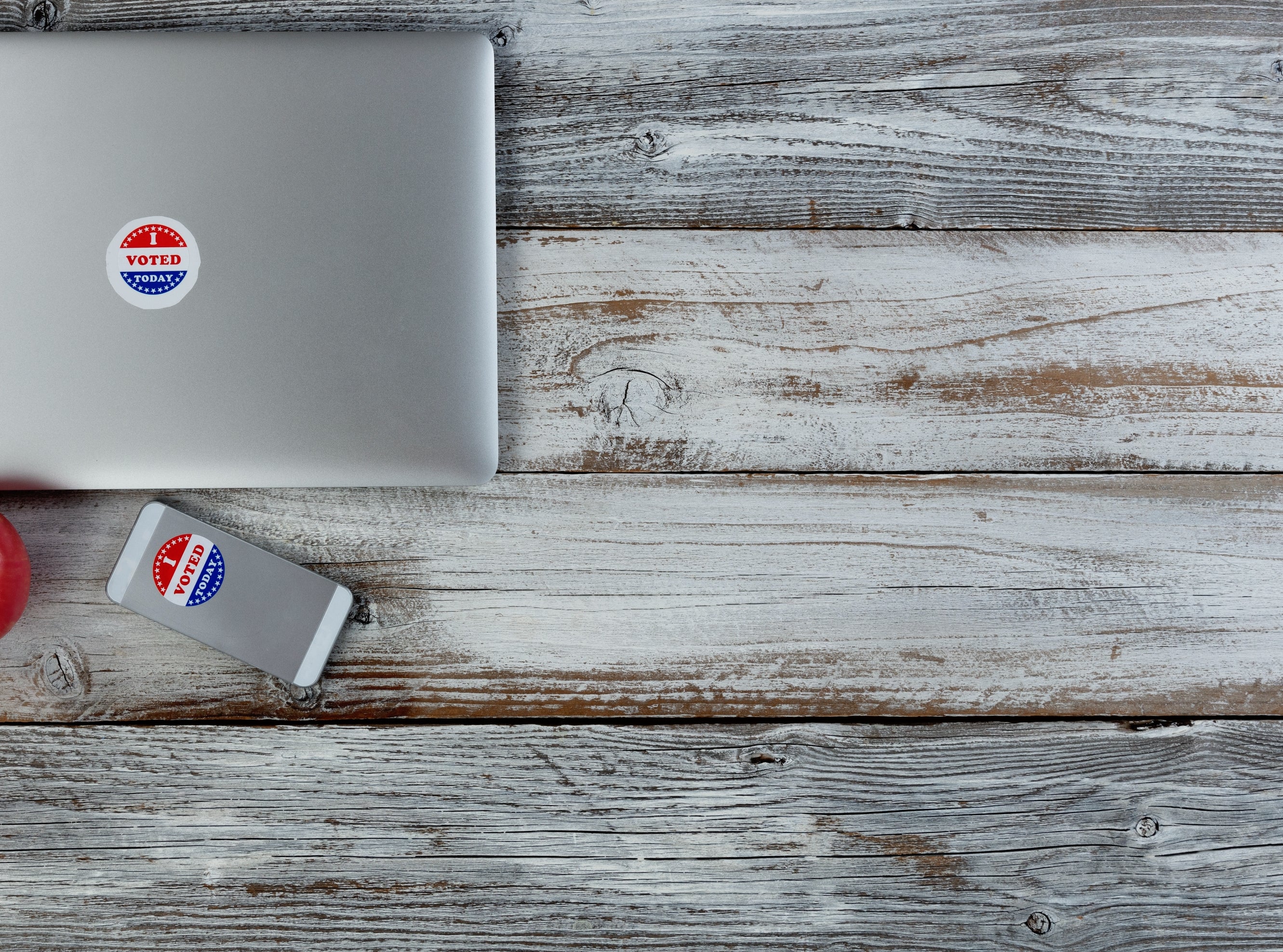 Laptop and telephone  with "I Voted" stickers adjacent  to an pome  connected  a woody  table