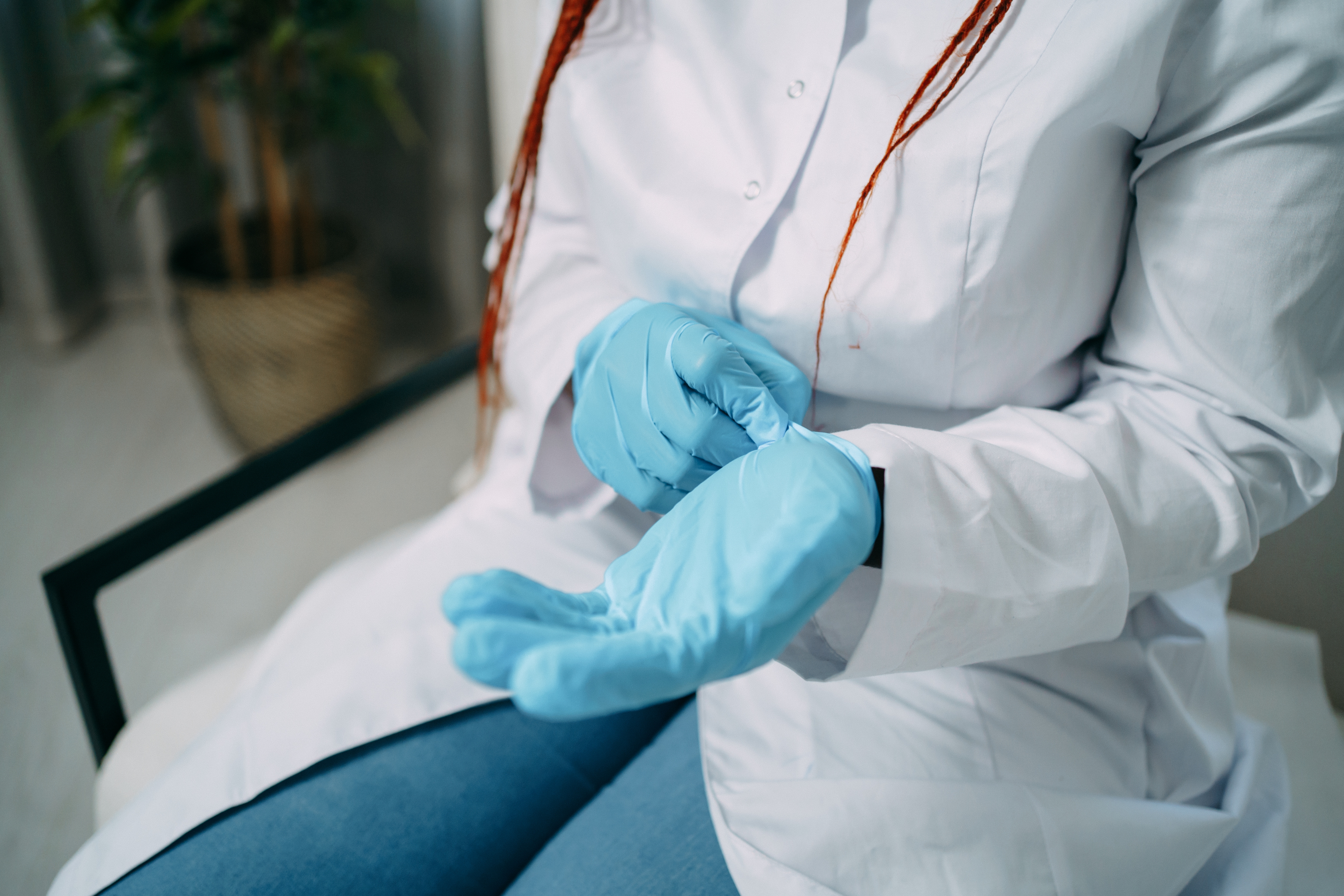 Person successful  a laboratory  overgarment  putting connected  bluish  gloves, sitting down. A works  is disposable   successful  the background