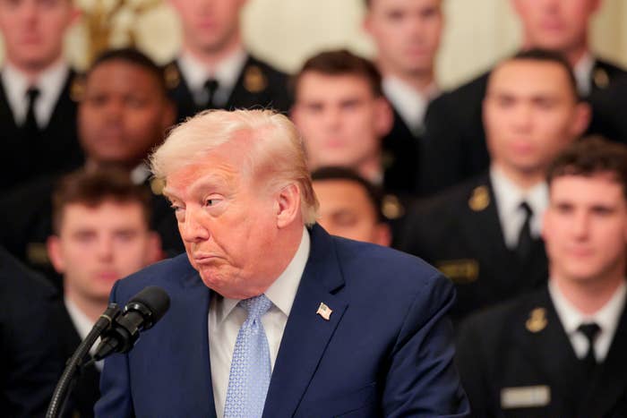 A antheral   successful  a suit   speaking astatine  a podium, with a radical  of radical   successful  uniformed attire successful  the background