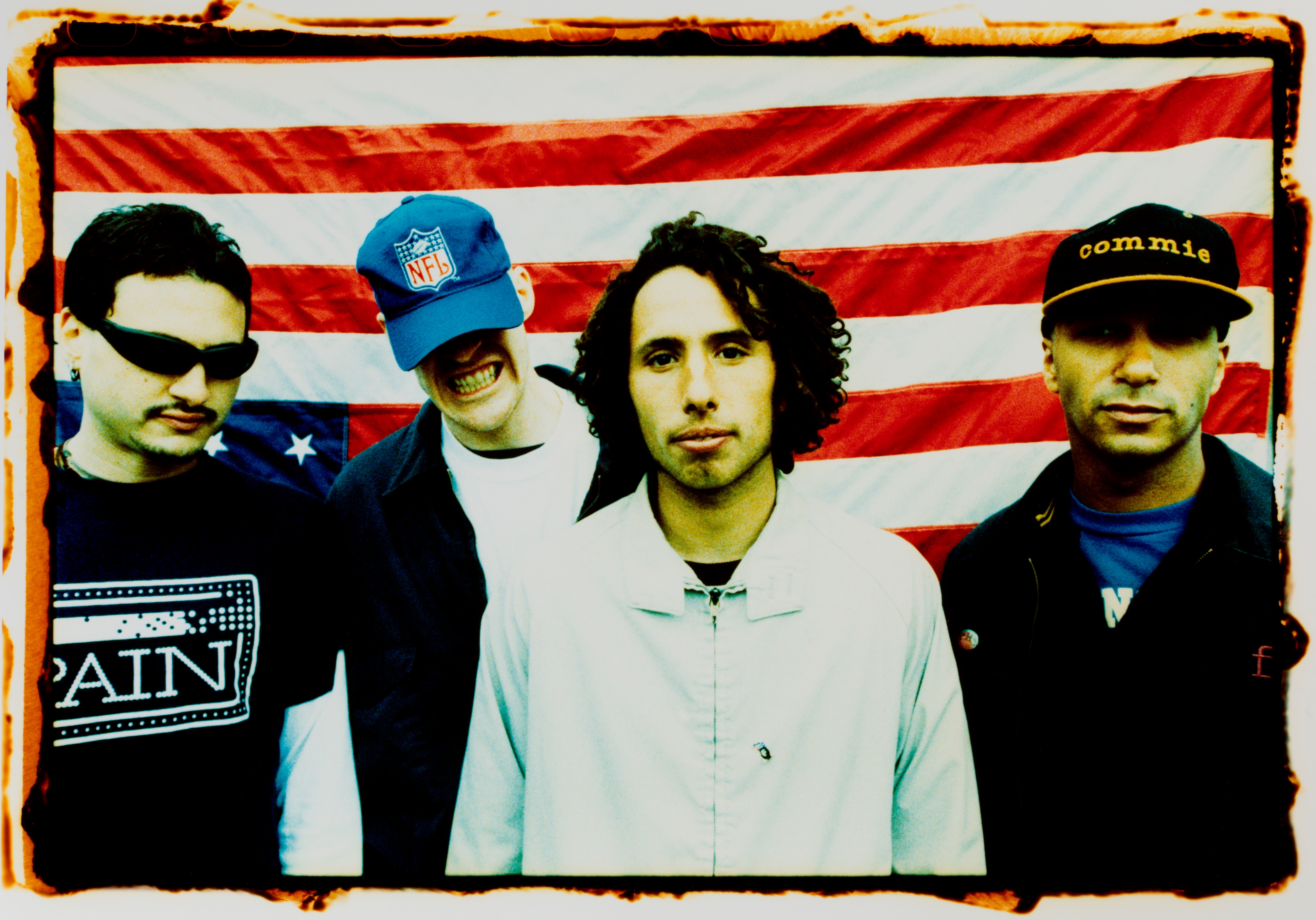 Four set members basal successful beforehand of a U.S. emblem backdrop, wearing casual 90s-style clothing, including T-shirts, hats, and a jacket