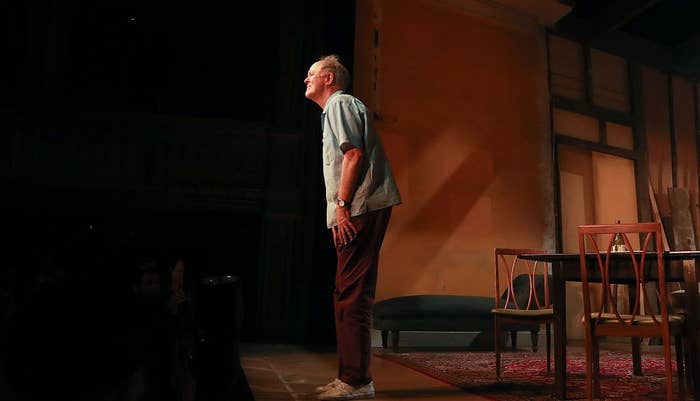 Person connected  signifier    performing, wearing a casual garment  and pants, with a melodramatic  acceptable   backdrop featuring chairs and a table