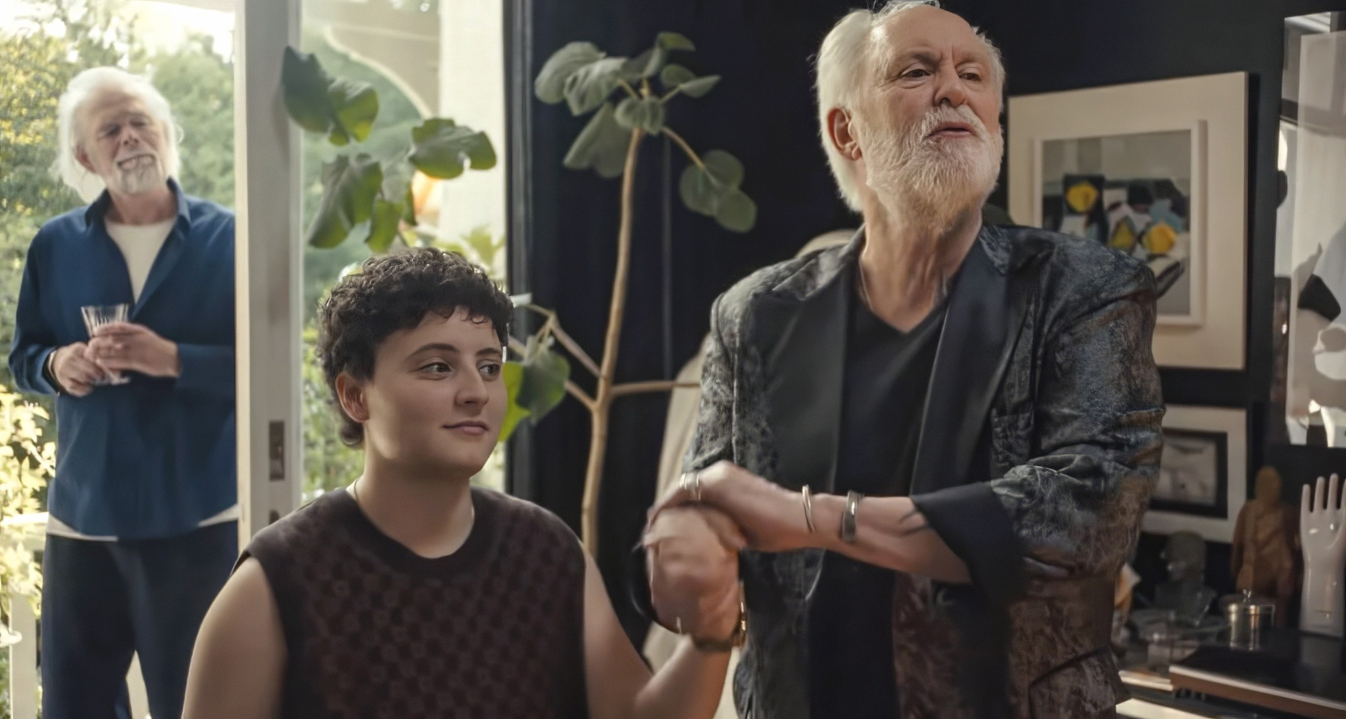 Three radical   successful  a room, with 1  aged  antheral   wearing a stylish jacket, holding hands with a younger idiosyncratic   sitting nearby