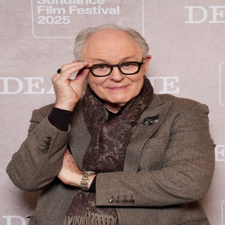 Person in tweed jacket and patterned scarf adjusting glasses at Sundance Film Festival 2025 backdrop