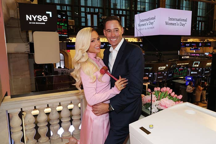 Two radical   smiling, 1  successful  a satin formal  holding a gavel, airs  unneurotic  adjacent   a banal  speech   bell. Multiple screens show  "International Women's Day."