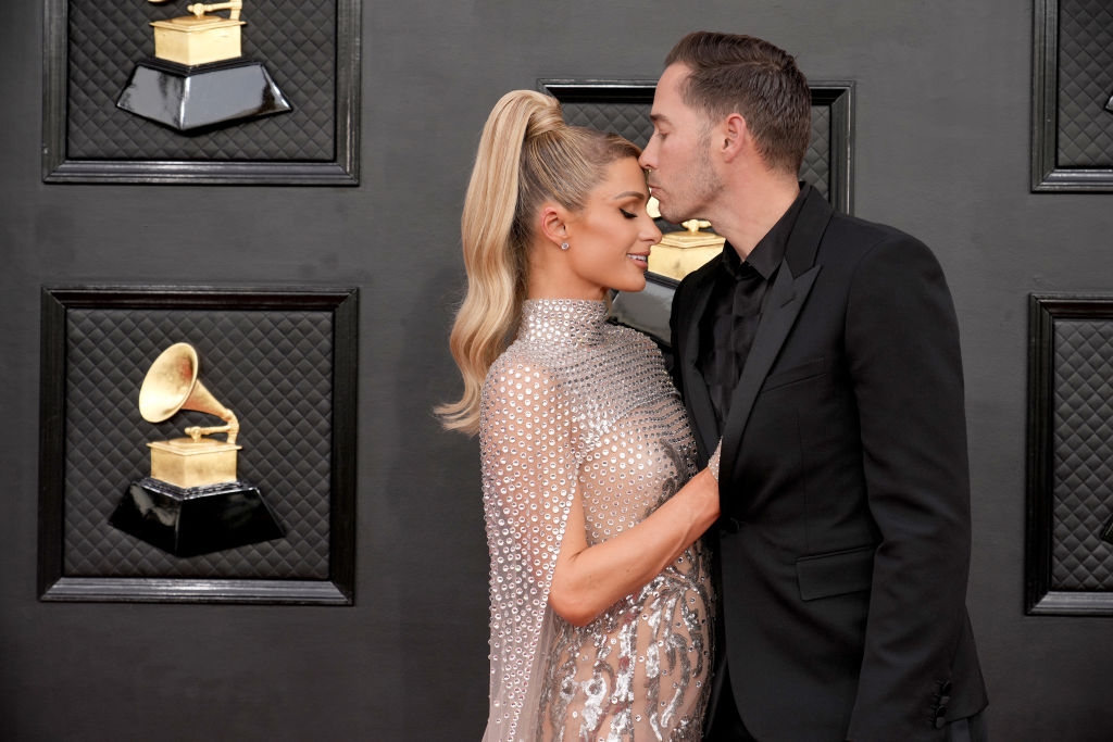 A mates poses connected the reddish carpet, 1 successful a shimmering sheer gown with beaded detail, the different successful a acheronian suit, sharing an affectionate moment
