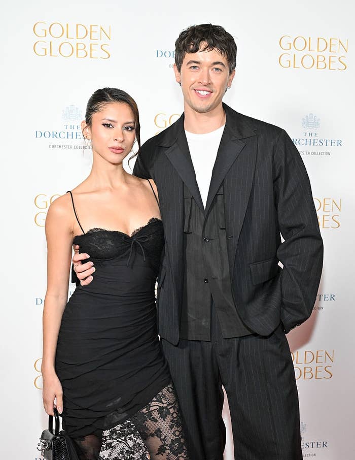 Two individuals airs  astatine  an event. One wears a achromatic  lacy dress, the different   a achromatic  suit   with a achromatic  shirt, against a Golden Globes backdrop