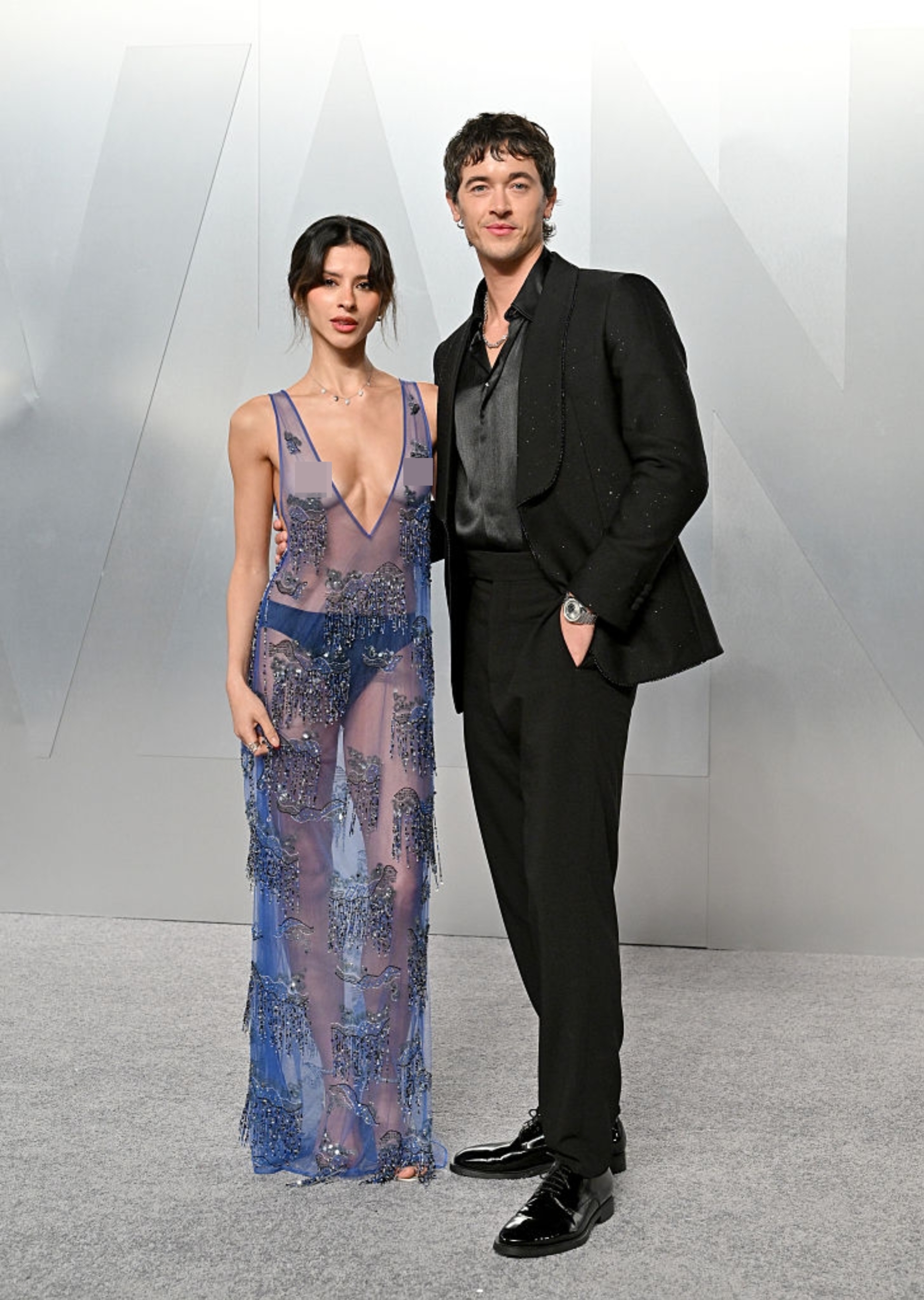 Two radical   airs  together; 1  wears a sheer gown with intricate detailing, the different   successful  a sleek, matching achromatic  suit