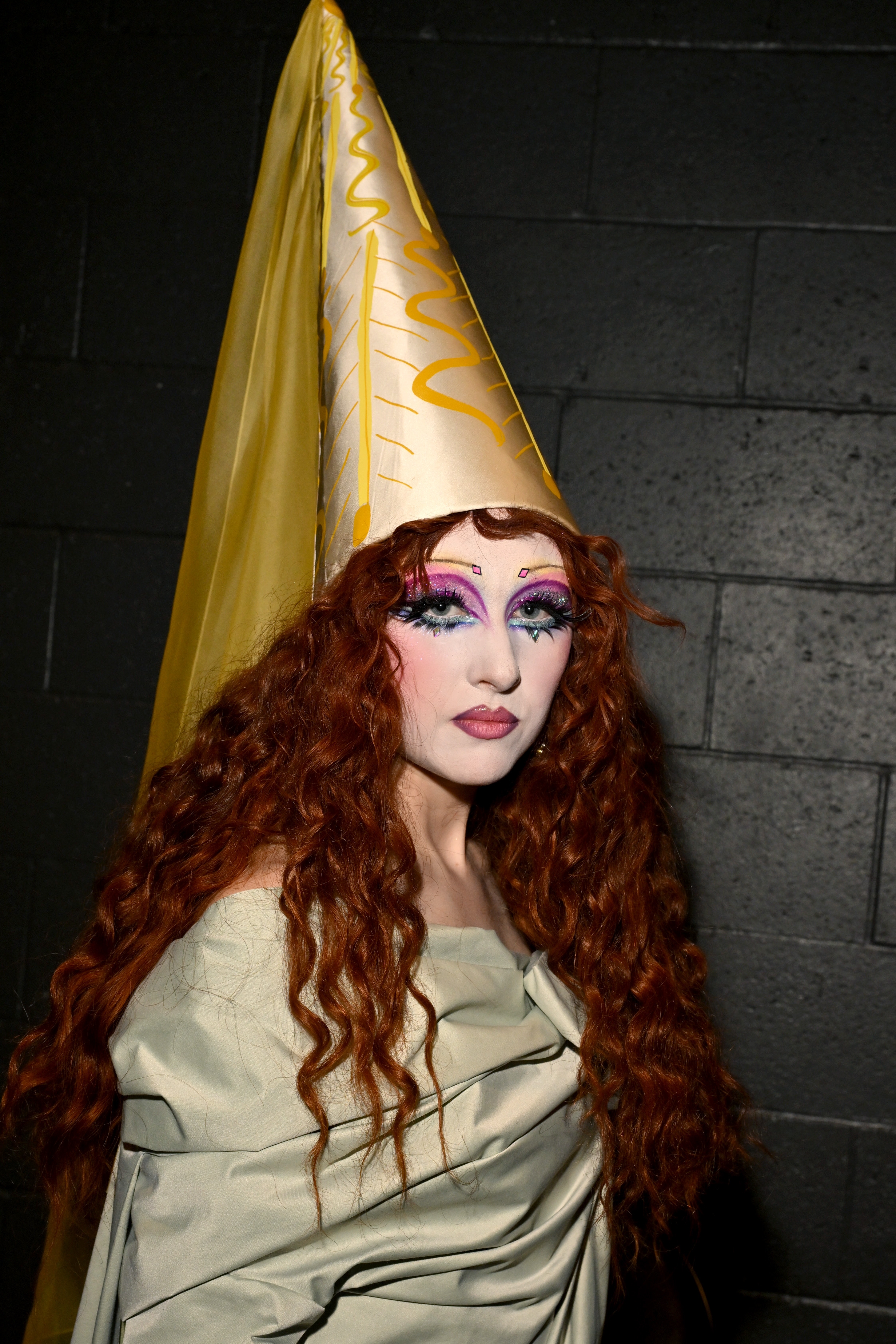 Chappell Roan with long, curly hairsbreadth  wearing a cone chapeau  and melodramatic  constitution  stands against a acheronian  background