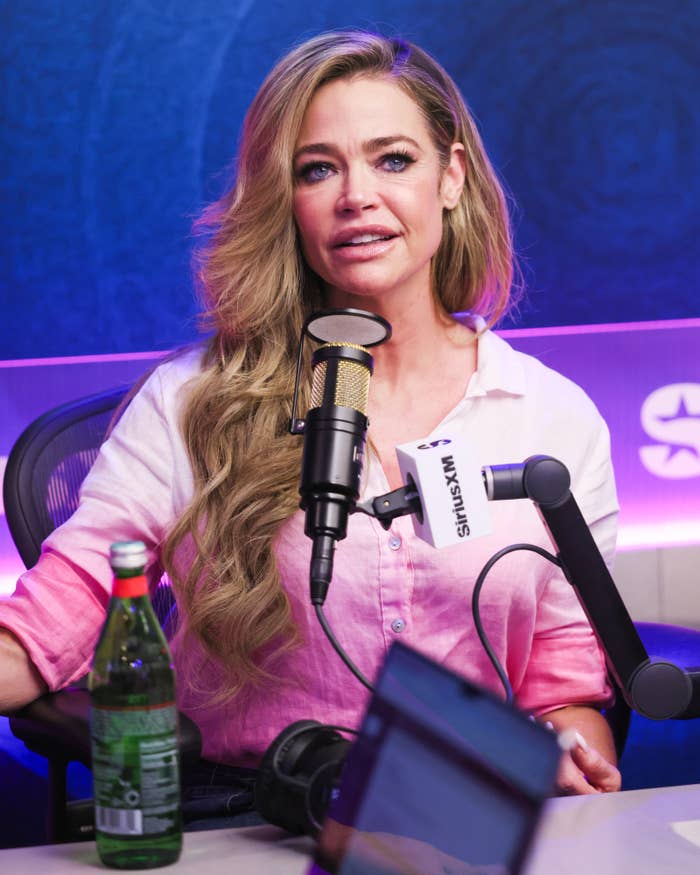 Denise Richards with agelong  wavy hairsbreadth  speaks into a microphone during a vigor   interview, wearing a casual button-up shirt